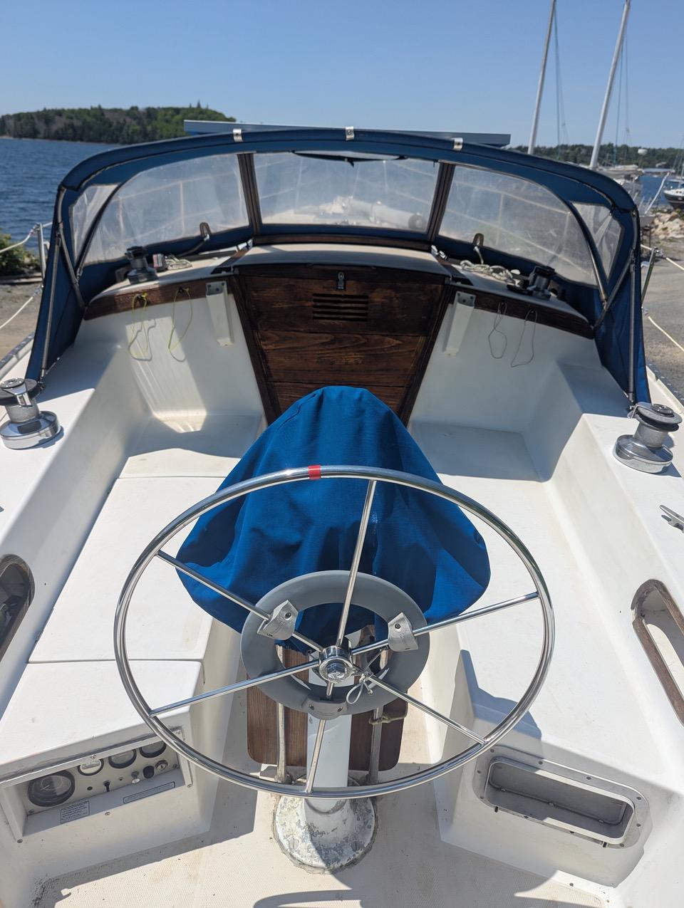 1985 Catalina 36 sailboat cockpit with steering wheel and blue cover, docked by the water.