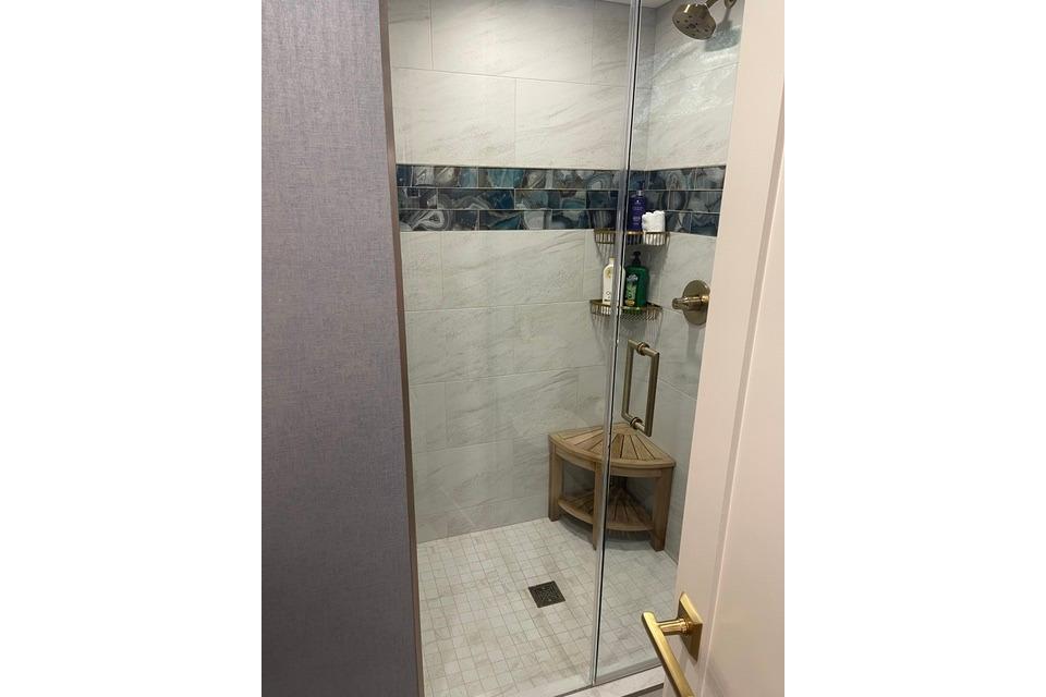 Modern shower with glass door, tiled walls, and corner shelf in Adonia's 2021 Queen Elizabeth model.