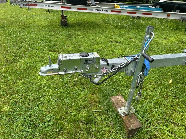 A boat trailer on grass with a hitch and safety chains.