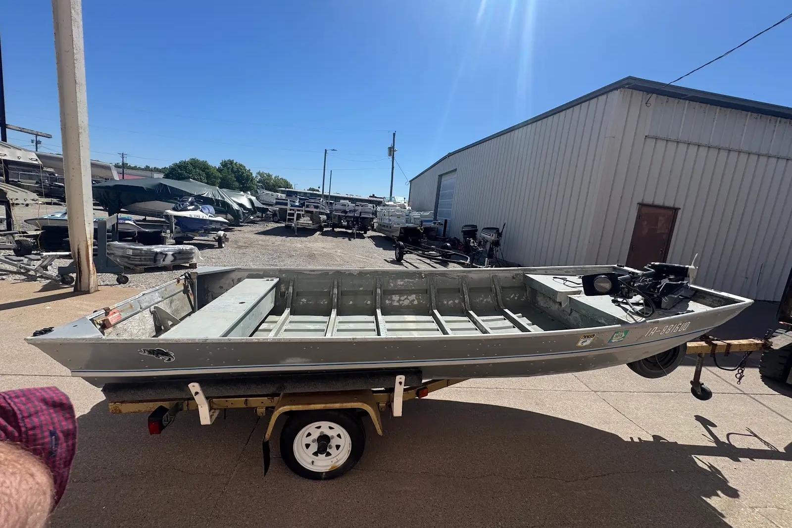 1973 Monark 14 Jon boat on trailer, parked outdoors under clear blue sky.