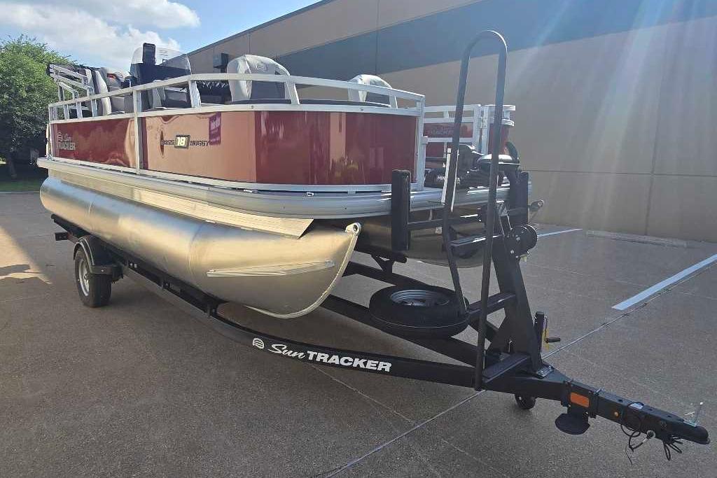 2026 Sun Tracker Bass Buggy 18 DLX pontoon boat on trailer in parking lot.