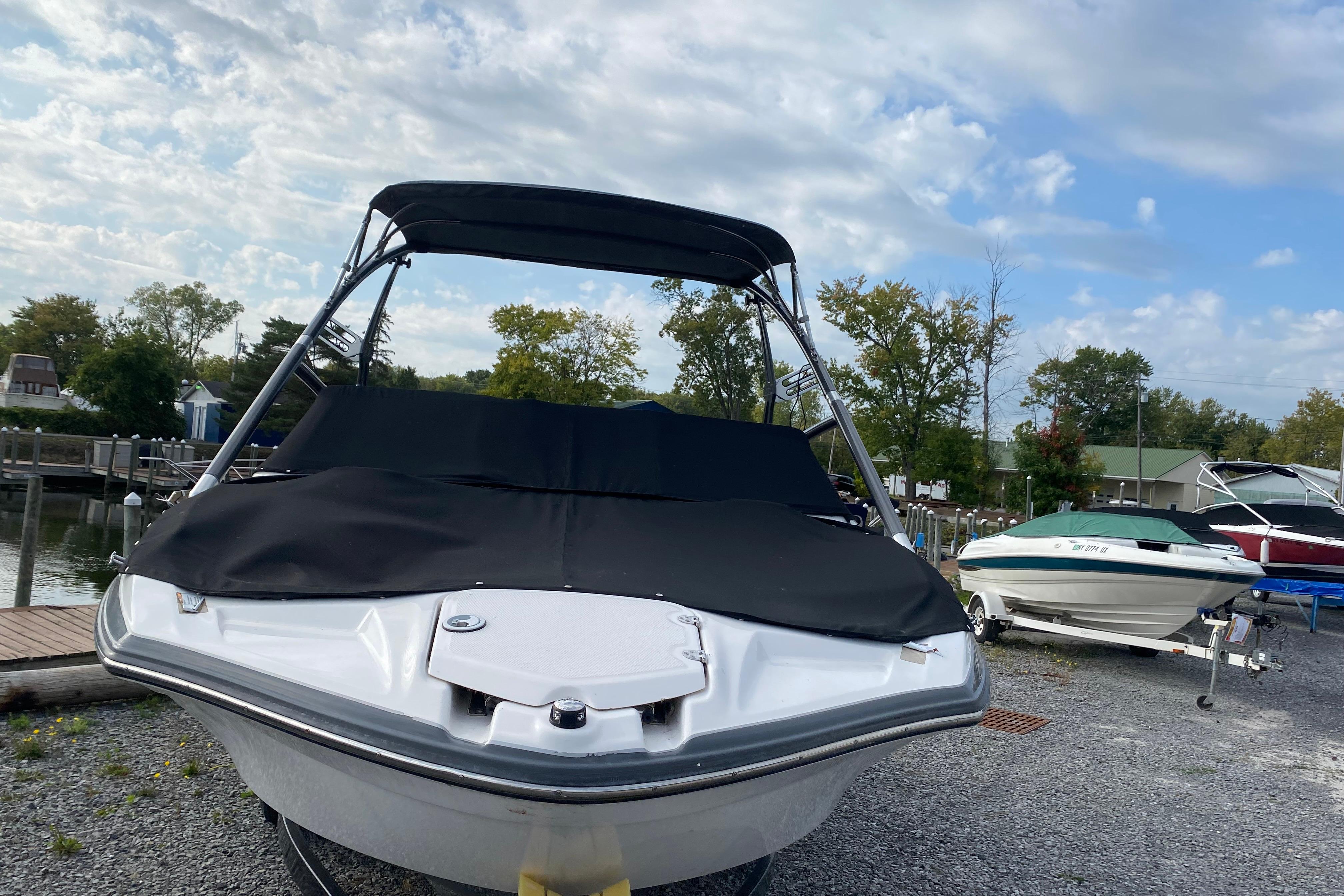2015 Yamaha Boats 212X with cover, parked on gravel near a dock.