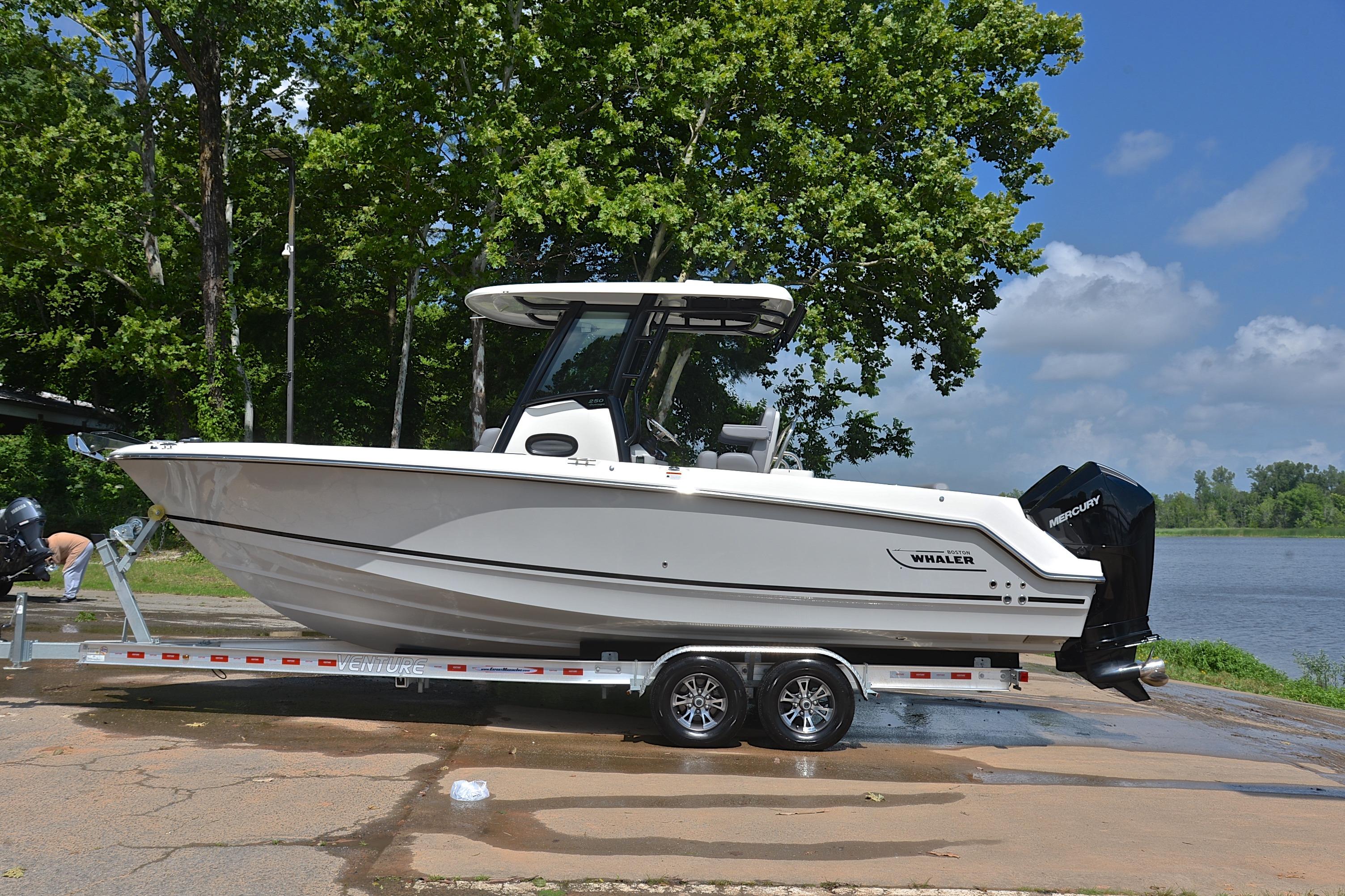 2024 Boston Whaler 250 Outrage boat on trailer by a lake, surrounded by trees.