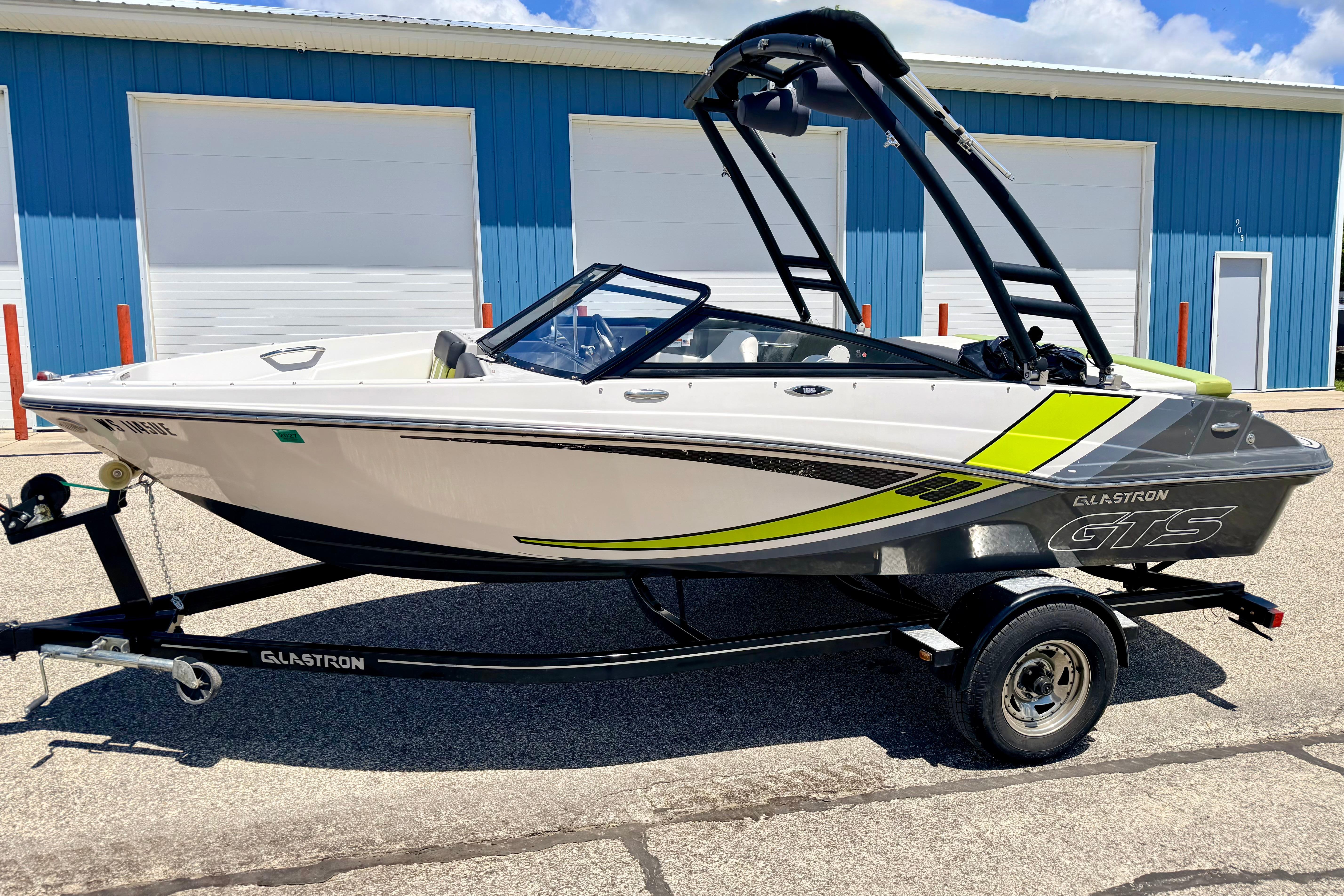 2018 Glastron GT 185 boat on trailer, parked near blue building.