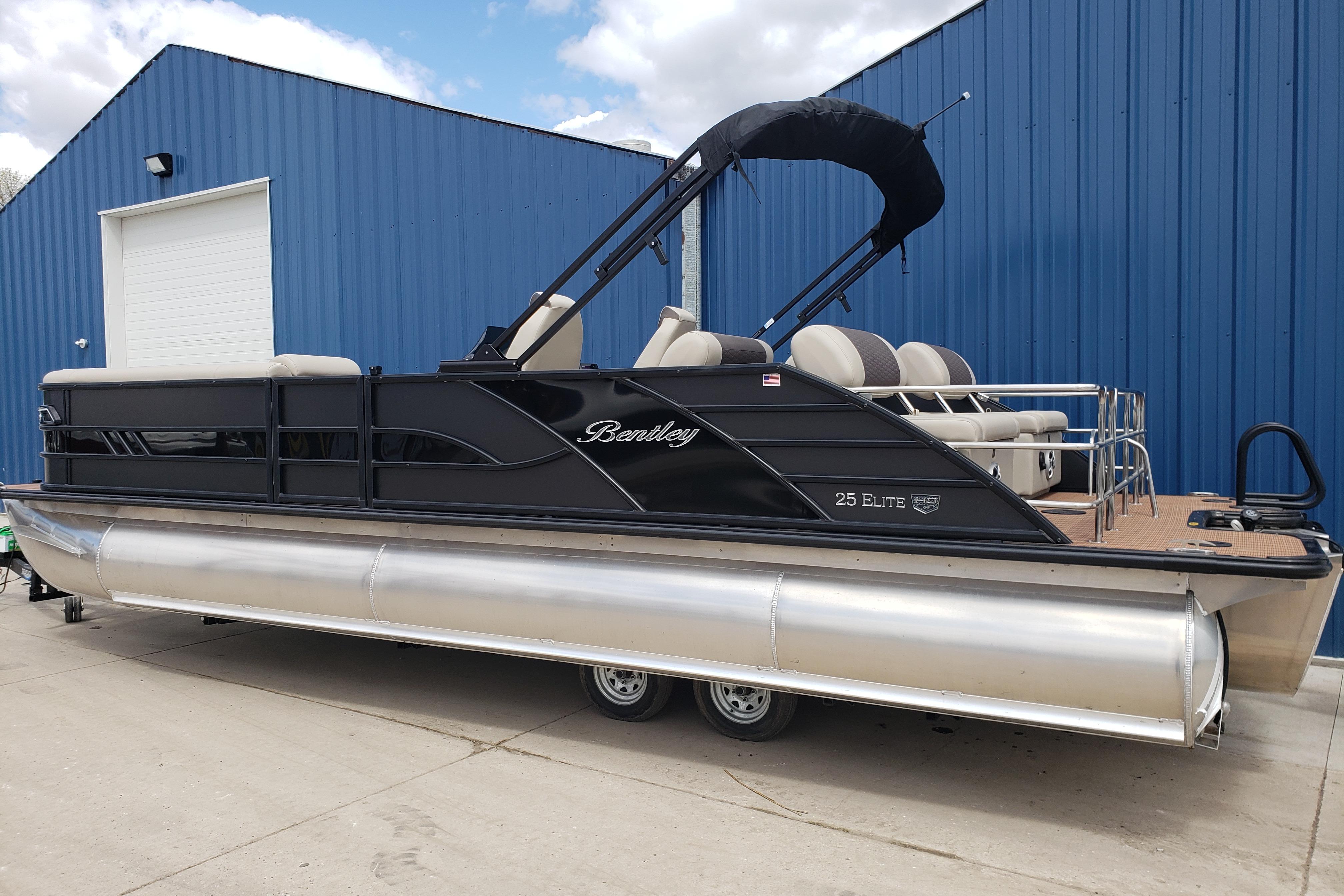 2026 Bentley Pontoons Elite 253 QSB pontoon boat parked by a blue building.