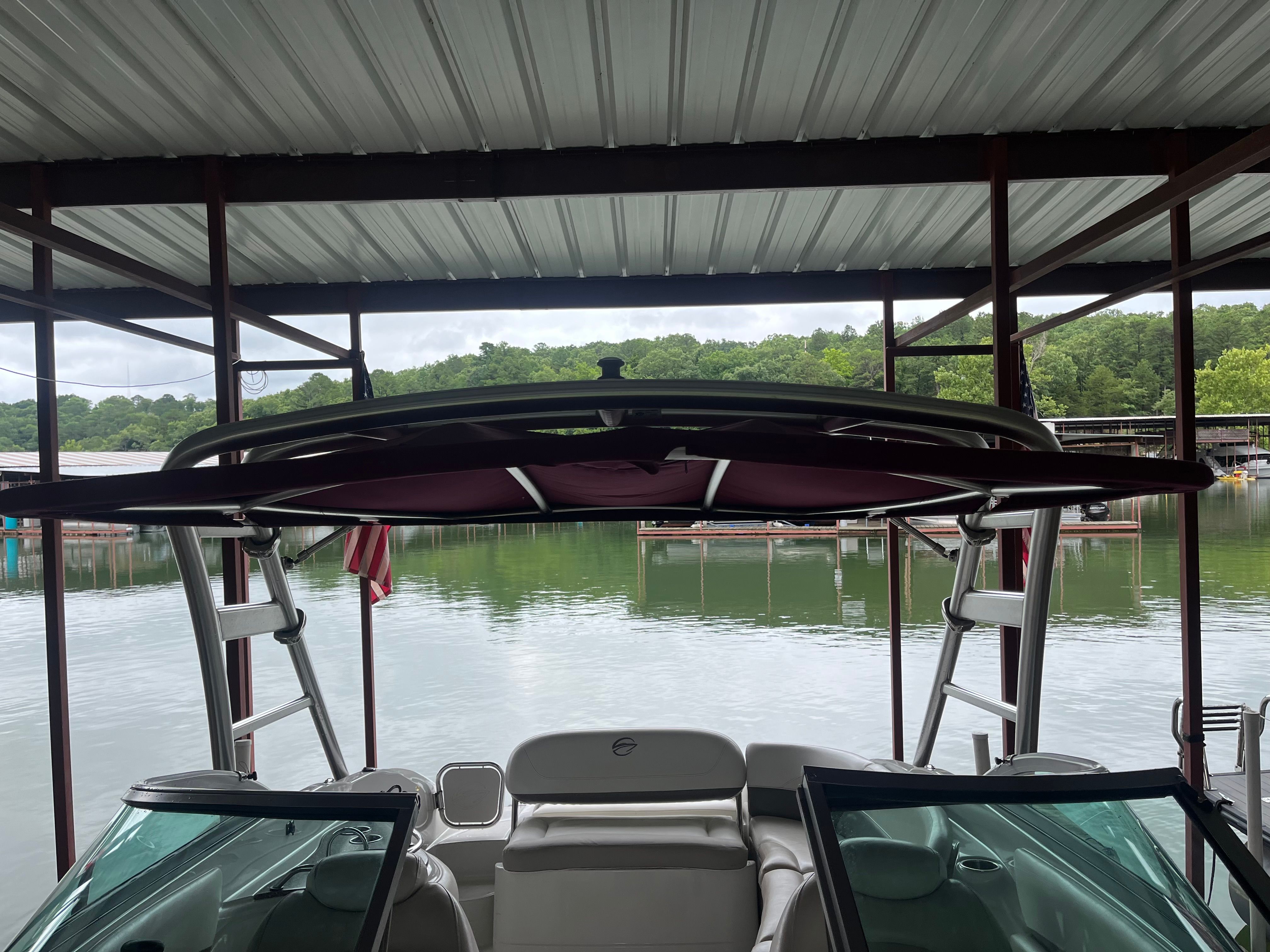 A 2008 Crownline 252EX boat is docked under a shelter, overlooking calm water.