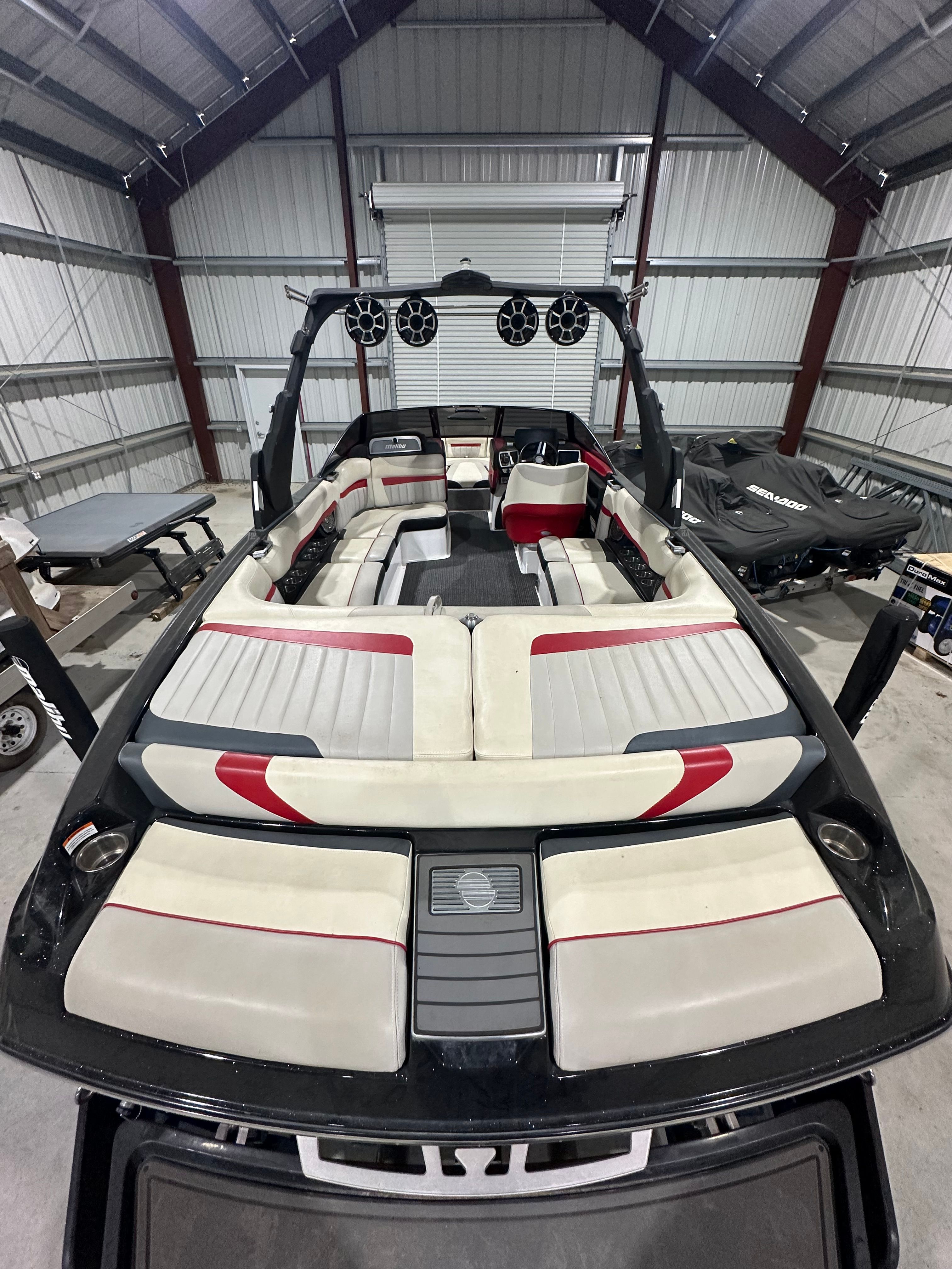 A Malibu Wakesetter 24 MXZ boat in a garage, featuring white and red seating.
