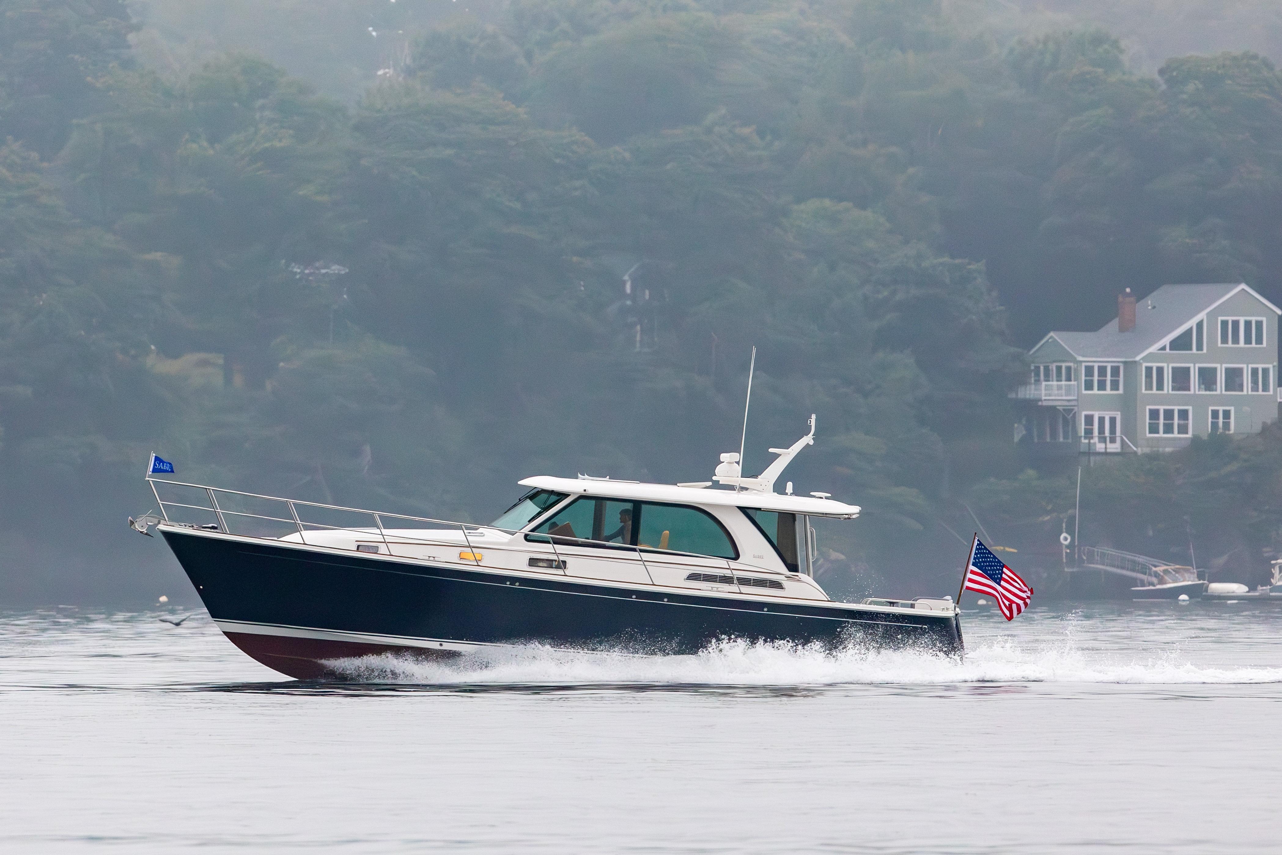 2027 Sabre 45 Salon Express cruising on a misty lake near shoreline homes.