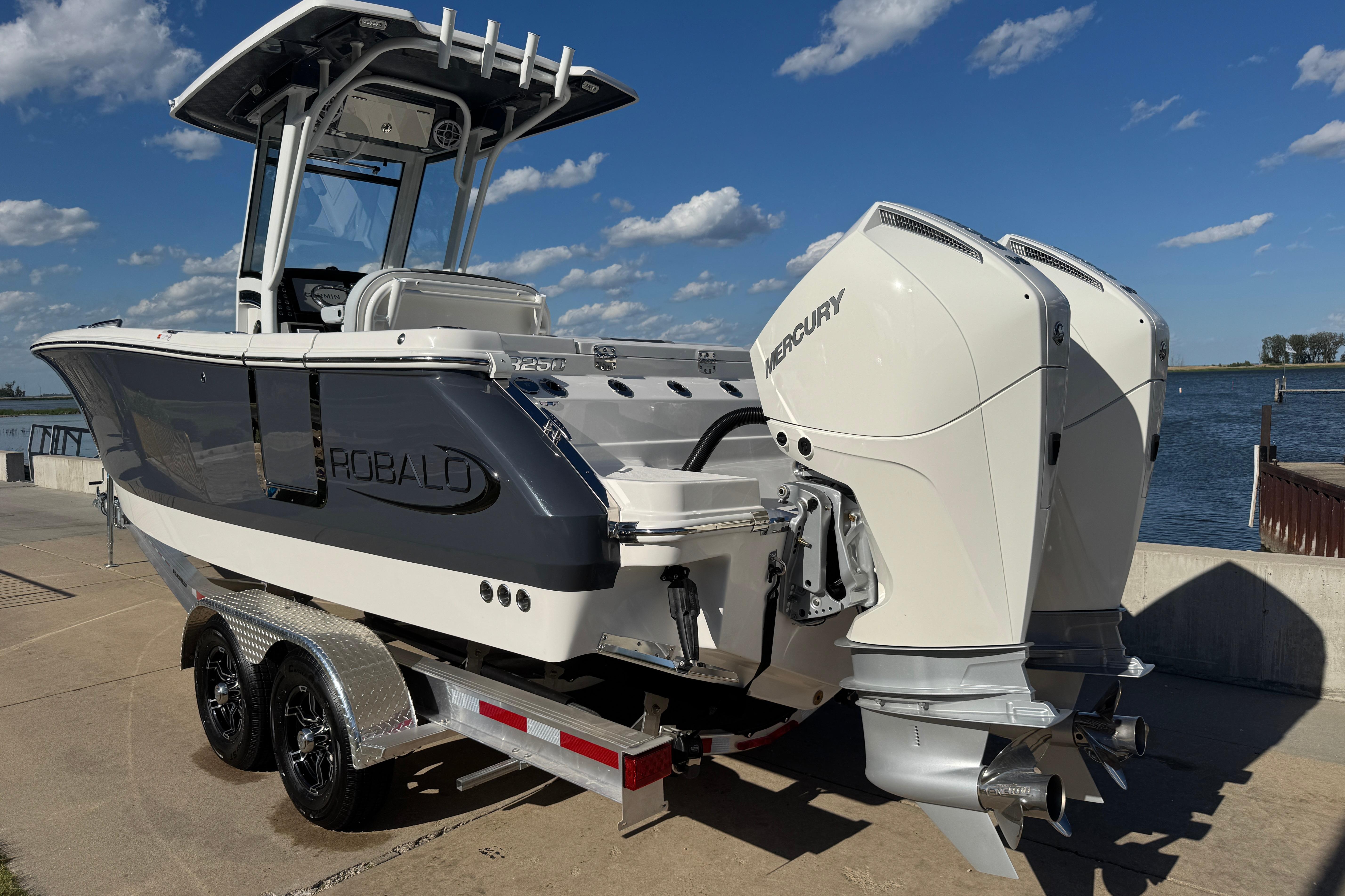 2026 Robalo R250 Center Console boat with dual Mercury engines on a trailer by the water.