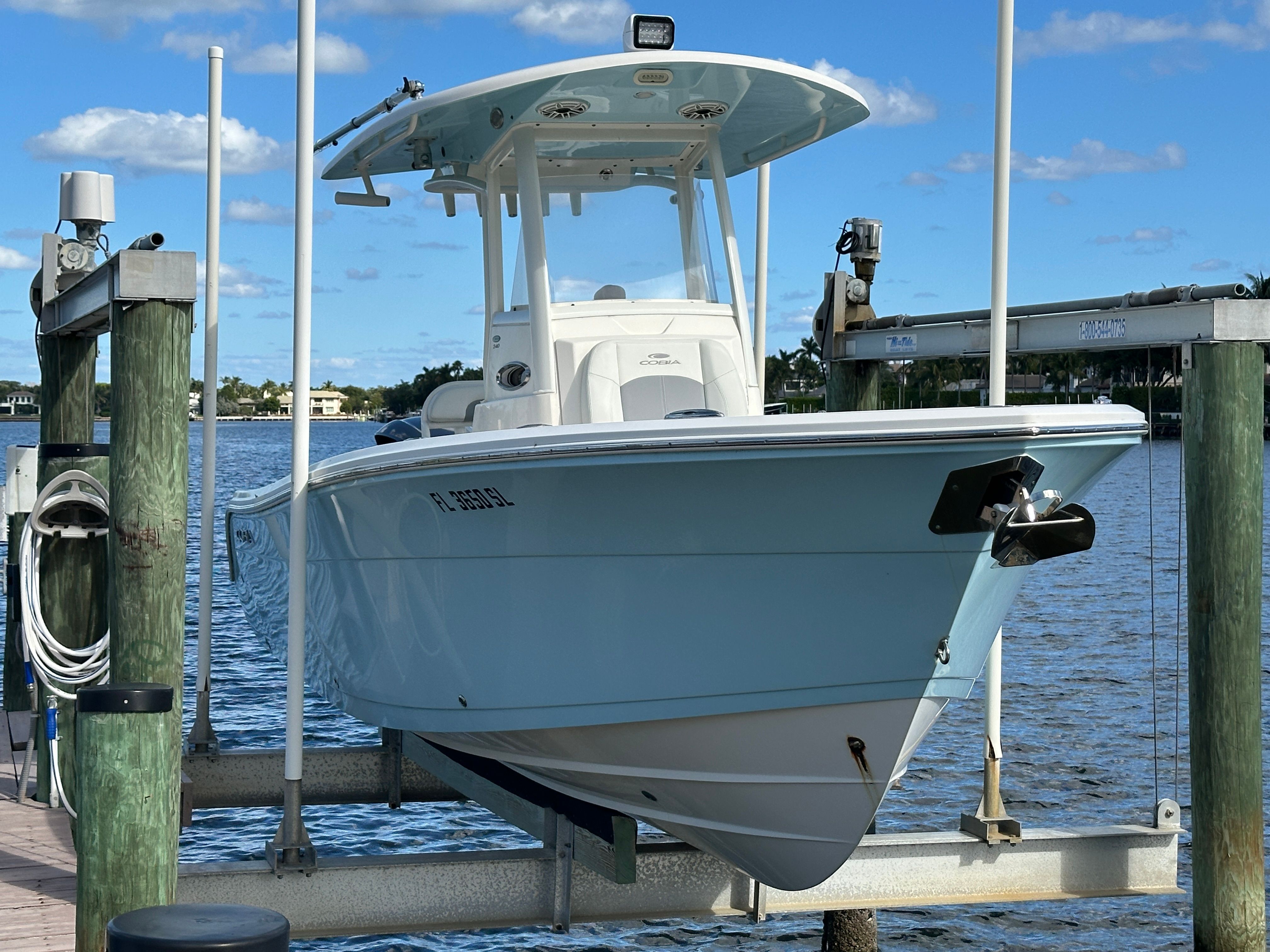A 2022 Cobia 240 Center Console boat is on a lift above the water. It features a light blue hull design.