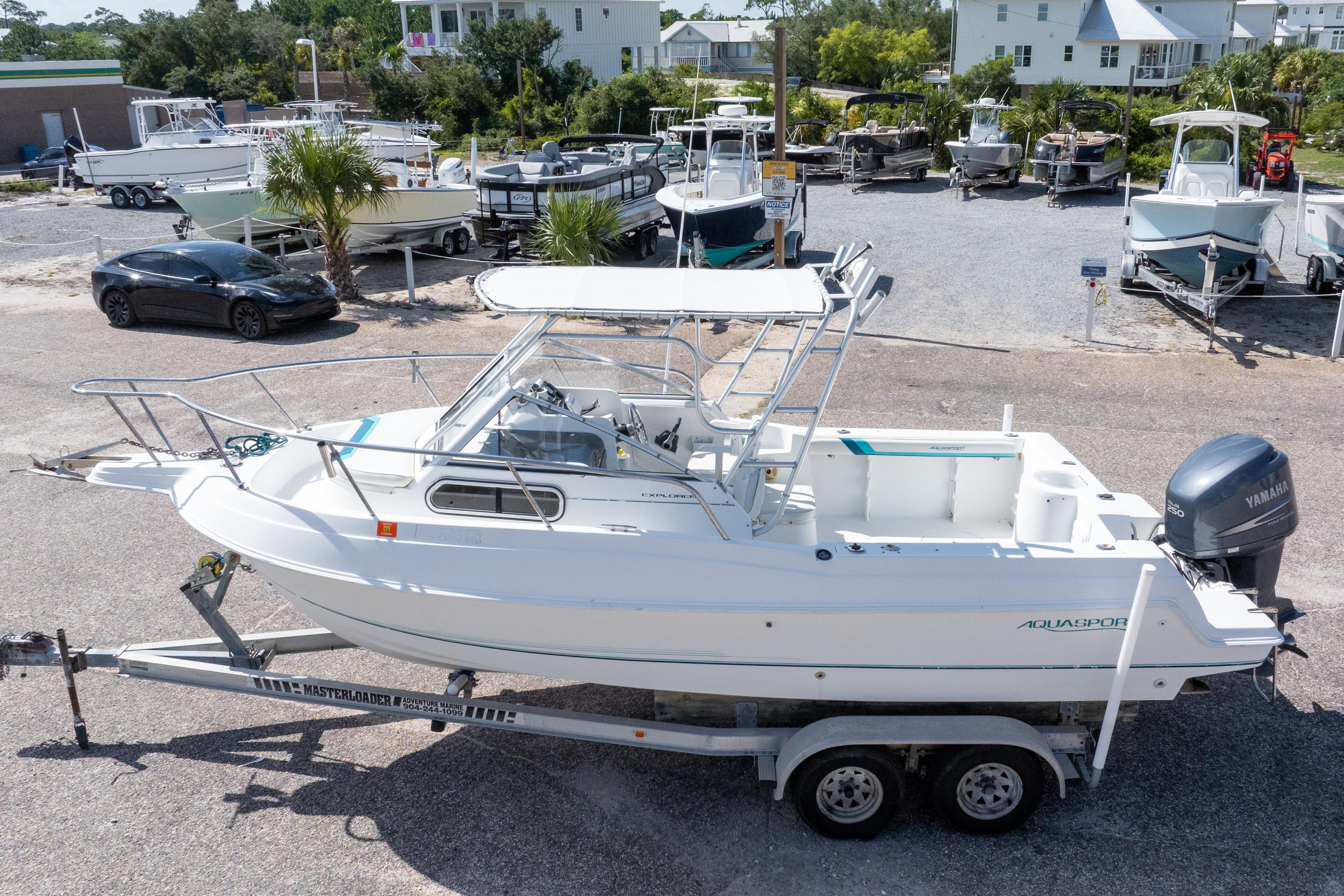 1999 Aquasport 225 Explorer boat on trailer, parked in a marina lot.