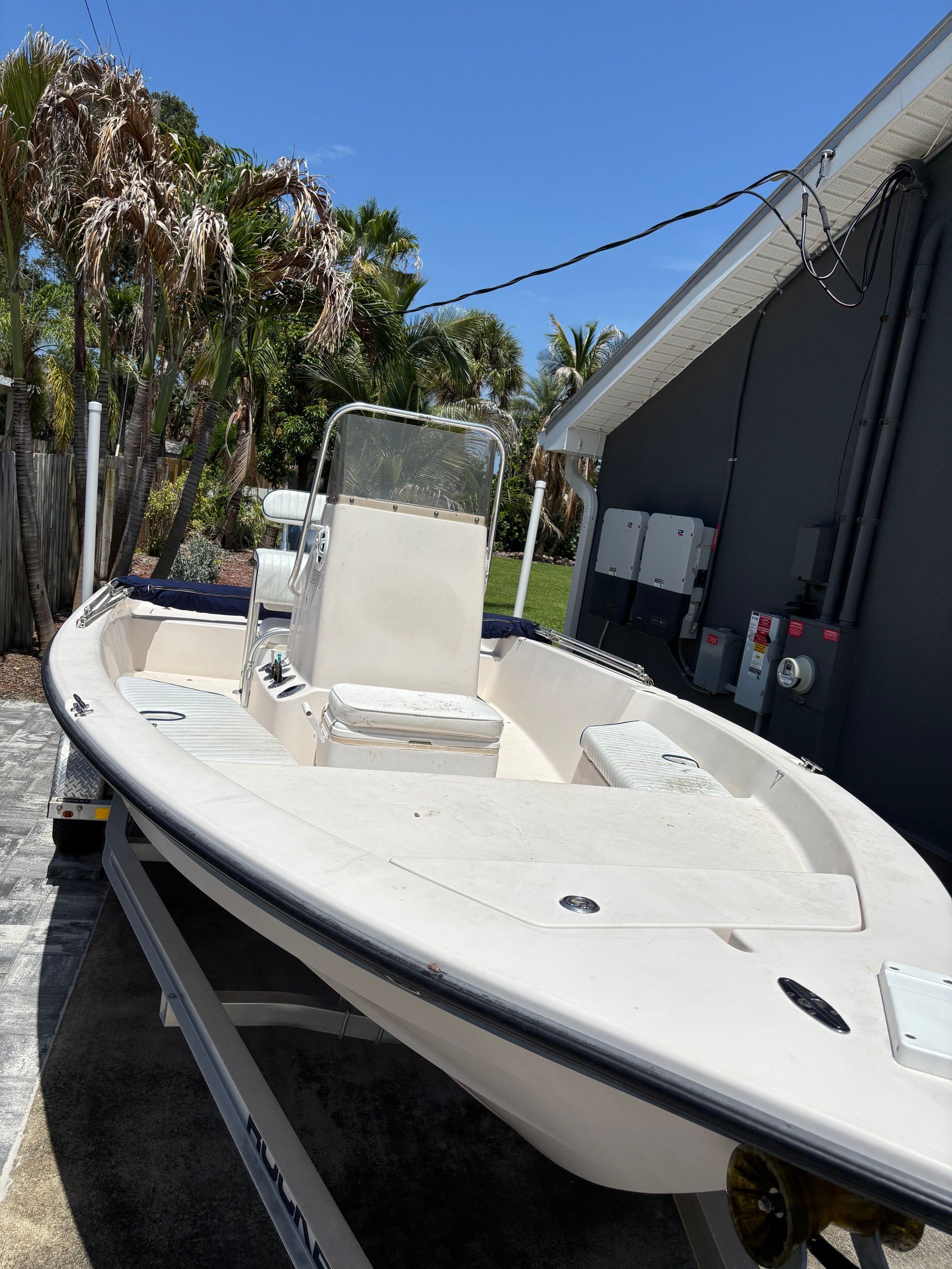 A white boat on a trailer with a console and seating. Palm trees in the background.