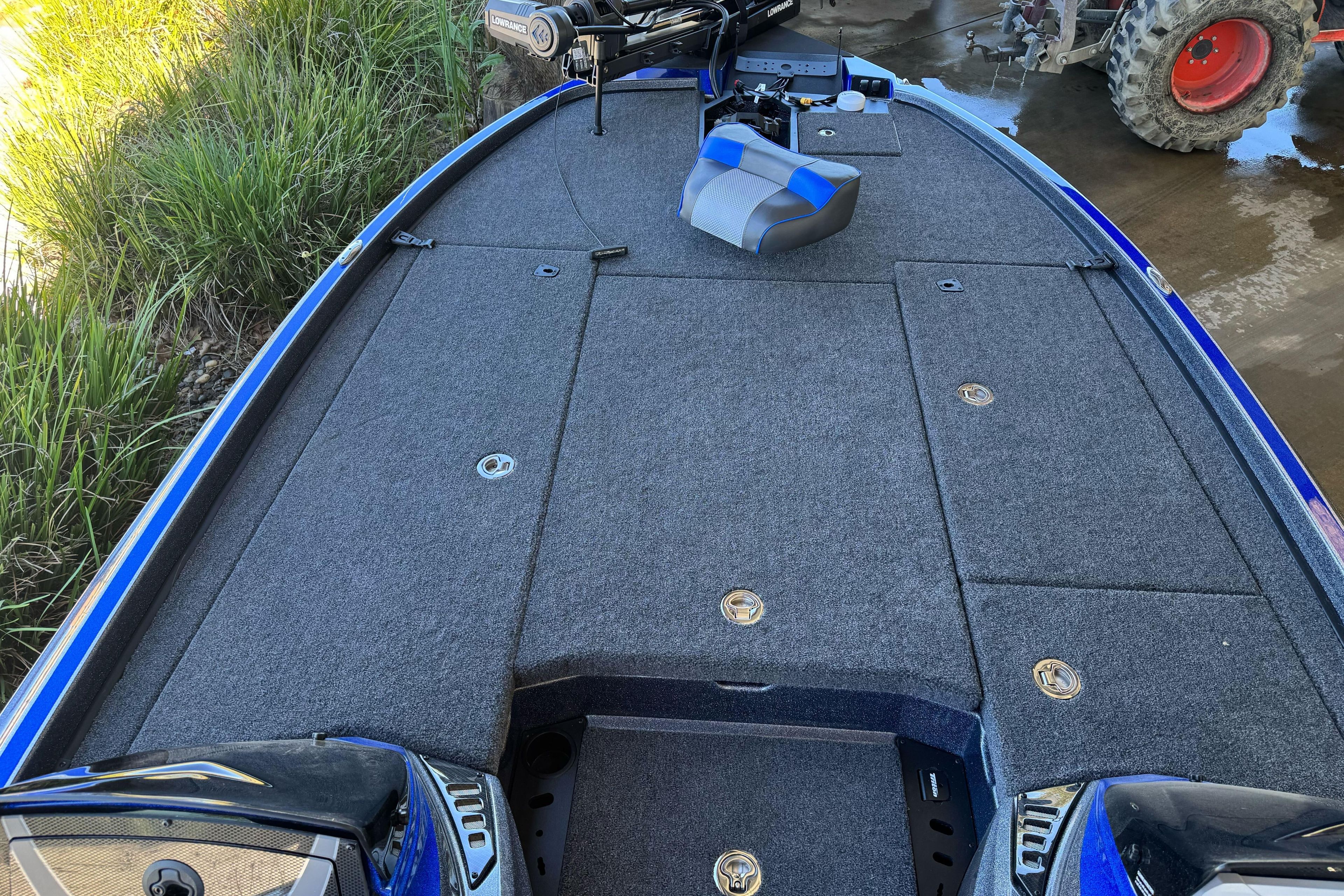 2026 Triton 21XP Patriot boat deck with Lowrance equipment, parked near grass and tractor.