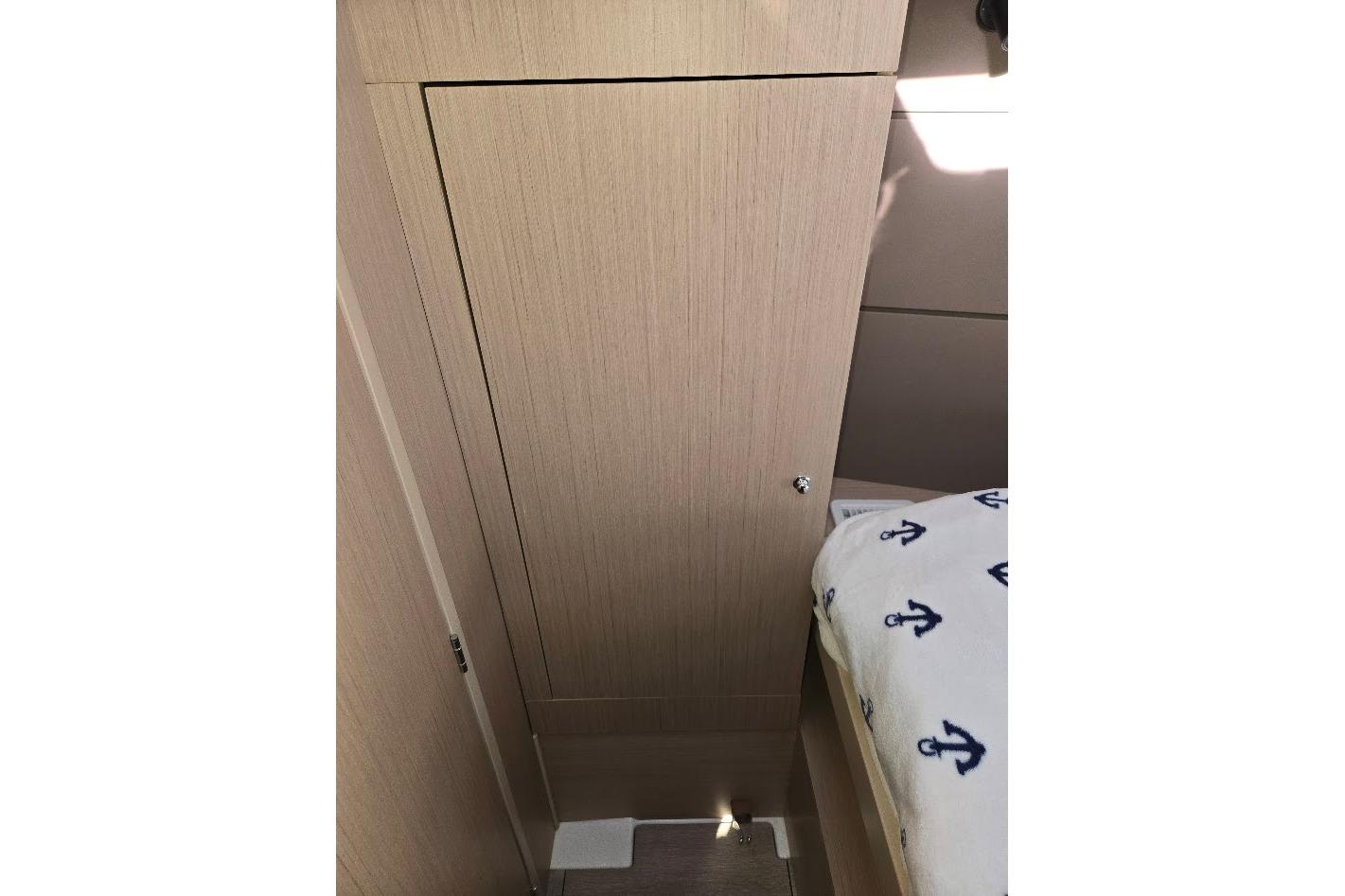 Interior of 2023 Beneteau Oceanis 38.1 yacht, featuring wooden cabinetry and anchor-patterned bedding.