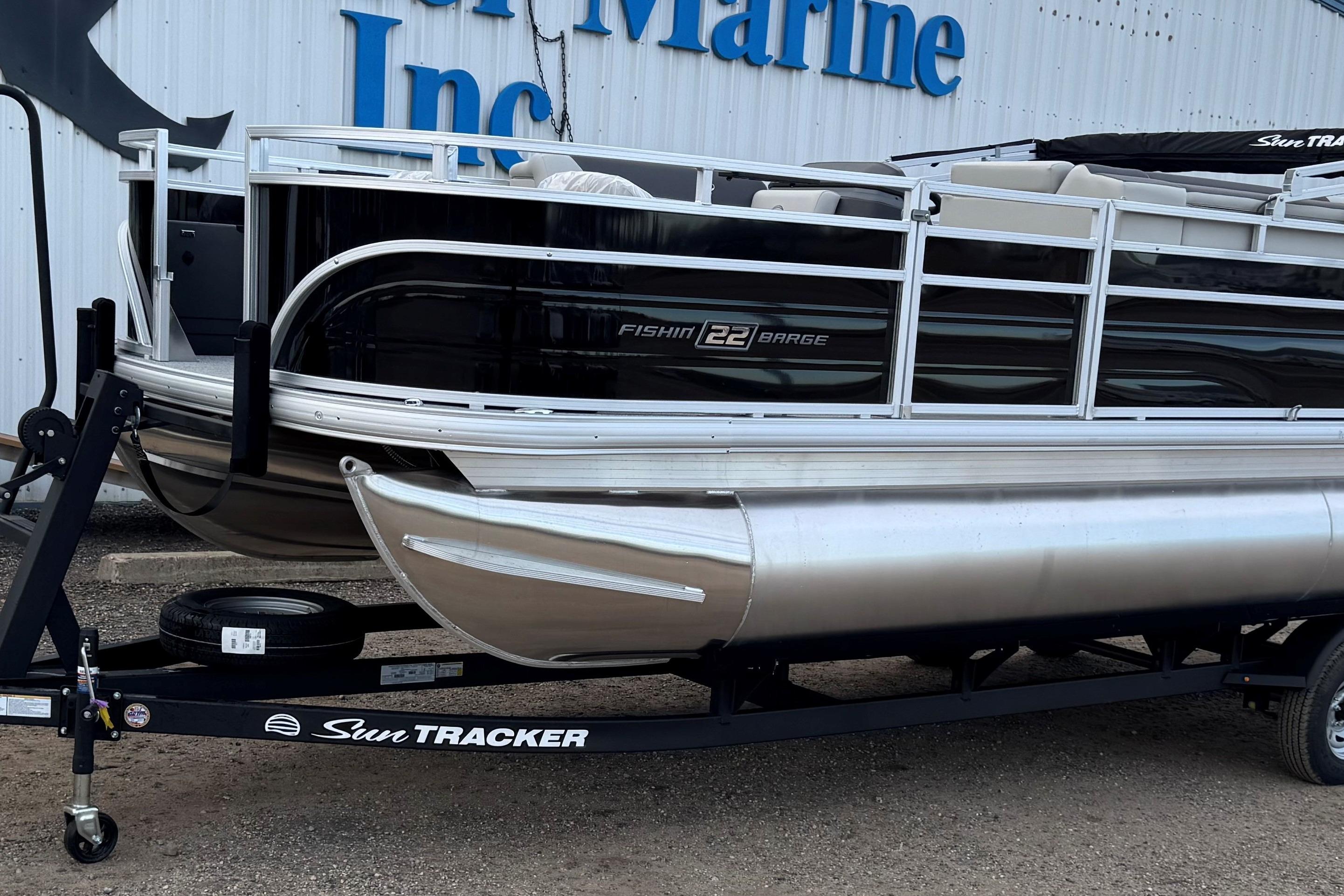 2026 Sun Tracker Fishin' Barge 22 DLX pontoon boat on trailer, parked outside.