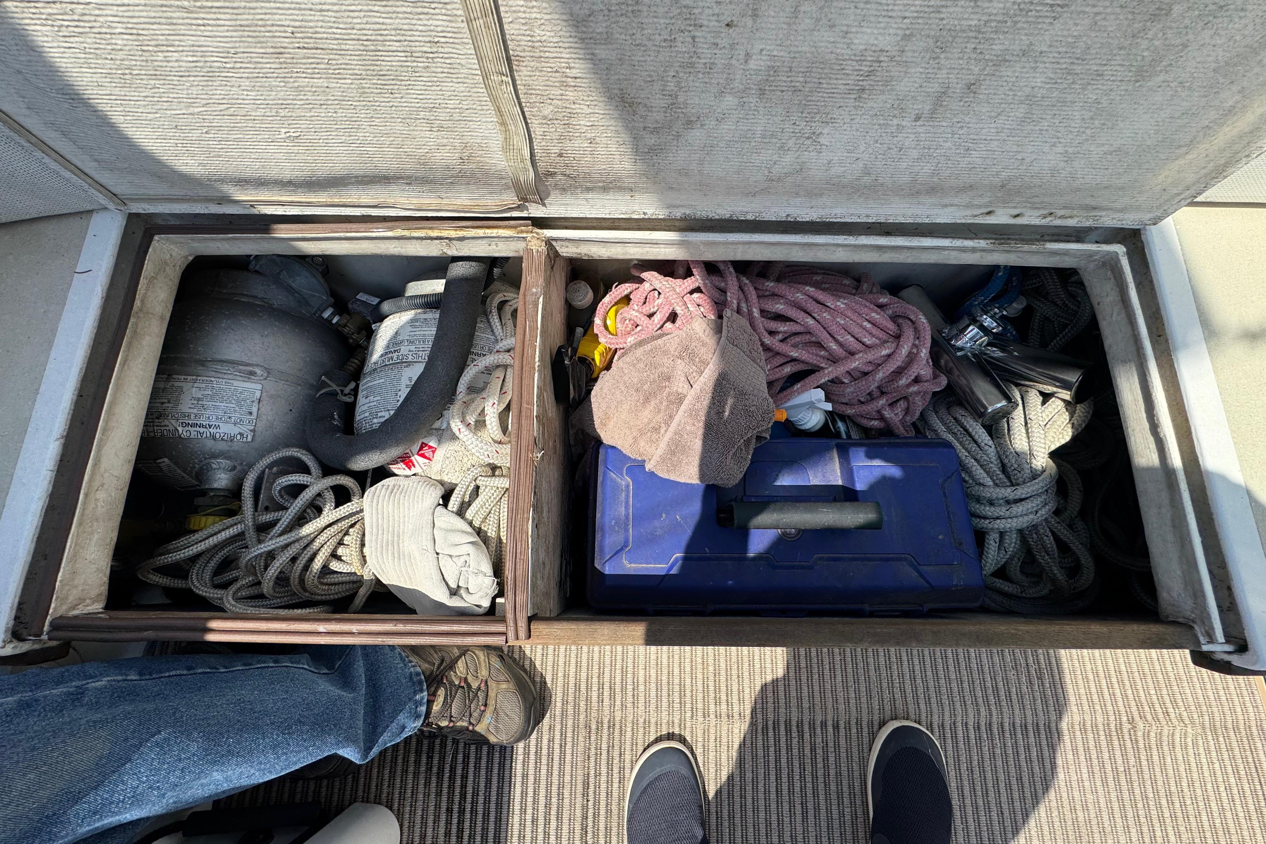An open storage compartment on a boat shows ropes, a blue toolbox, and a gas cylinder.