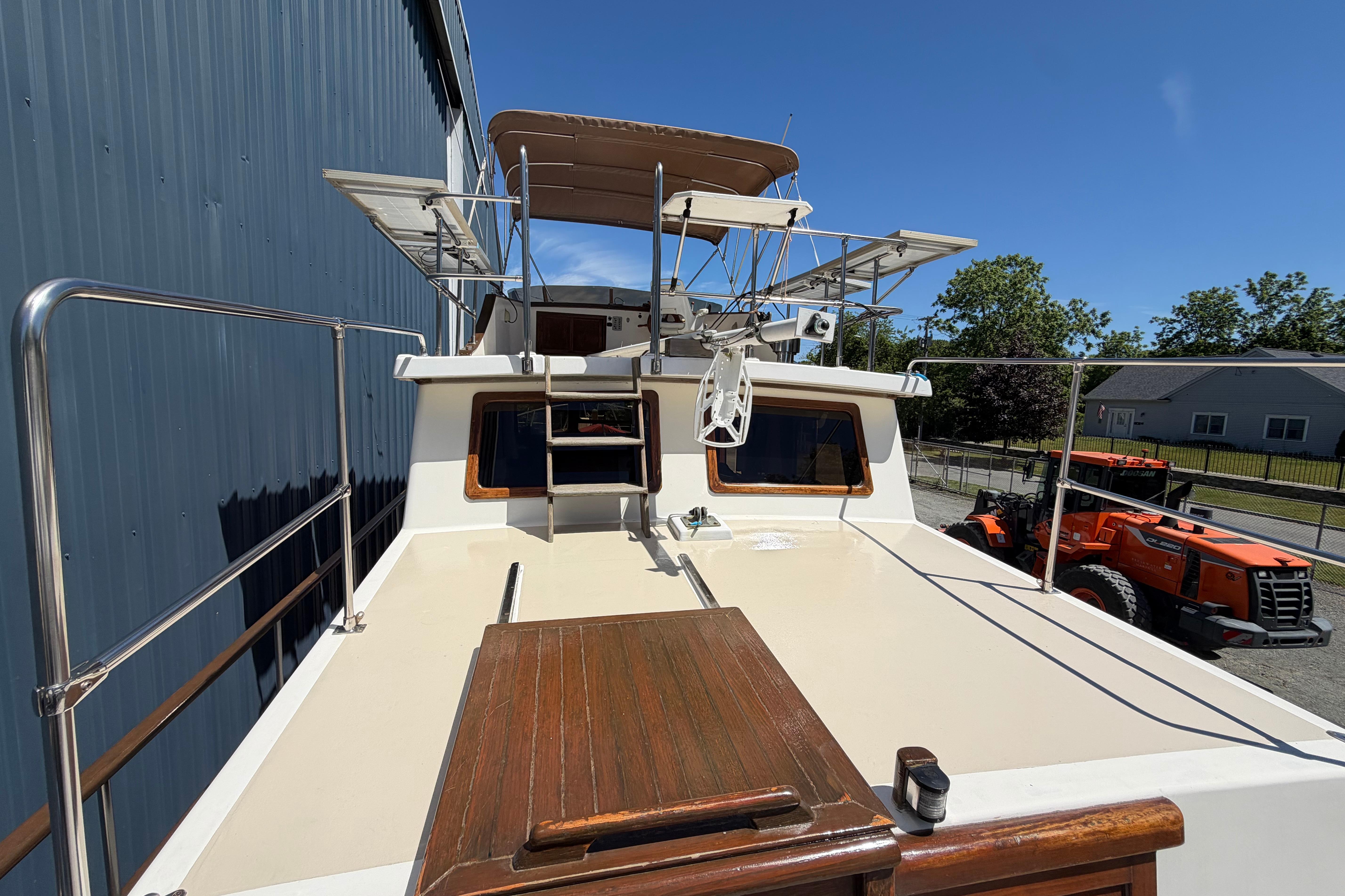1987 Marine Trader 36 yacht deck with railing, docked beside a building under clear blue sky.