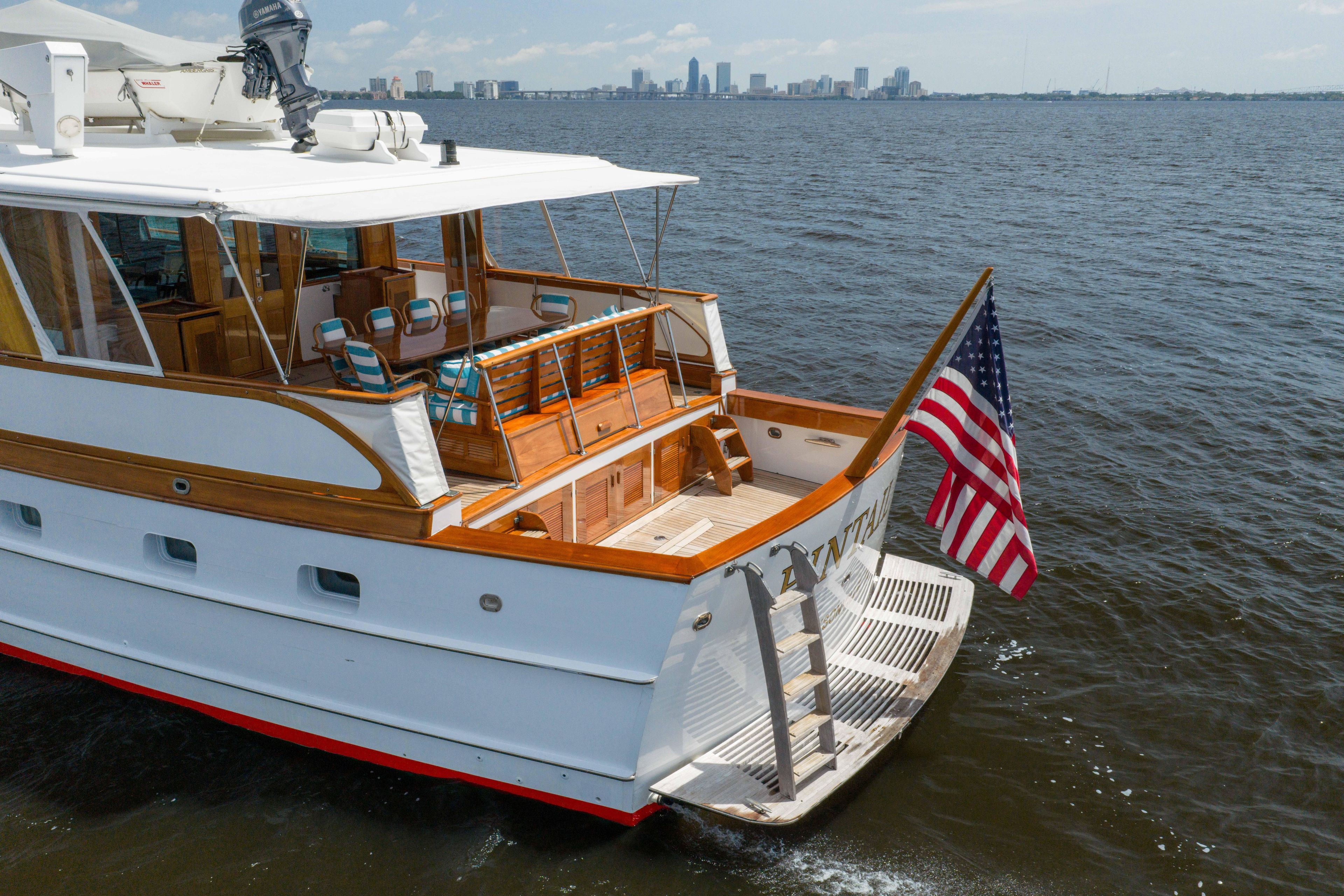 Classic 1963 Trumpy yacht with American flag, cruising near city skyline.