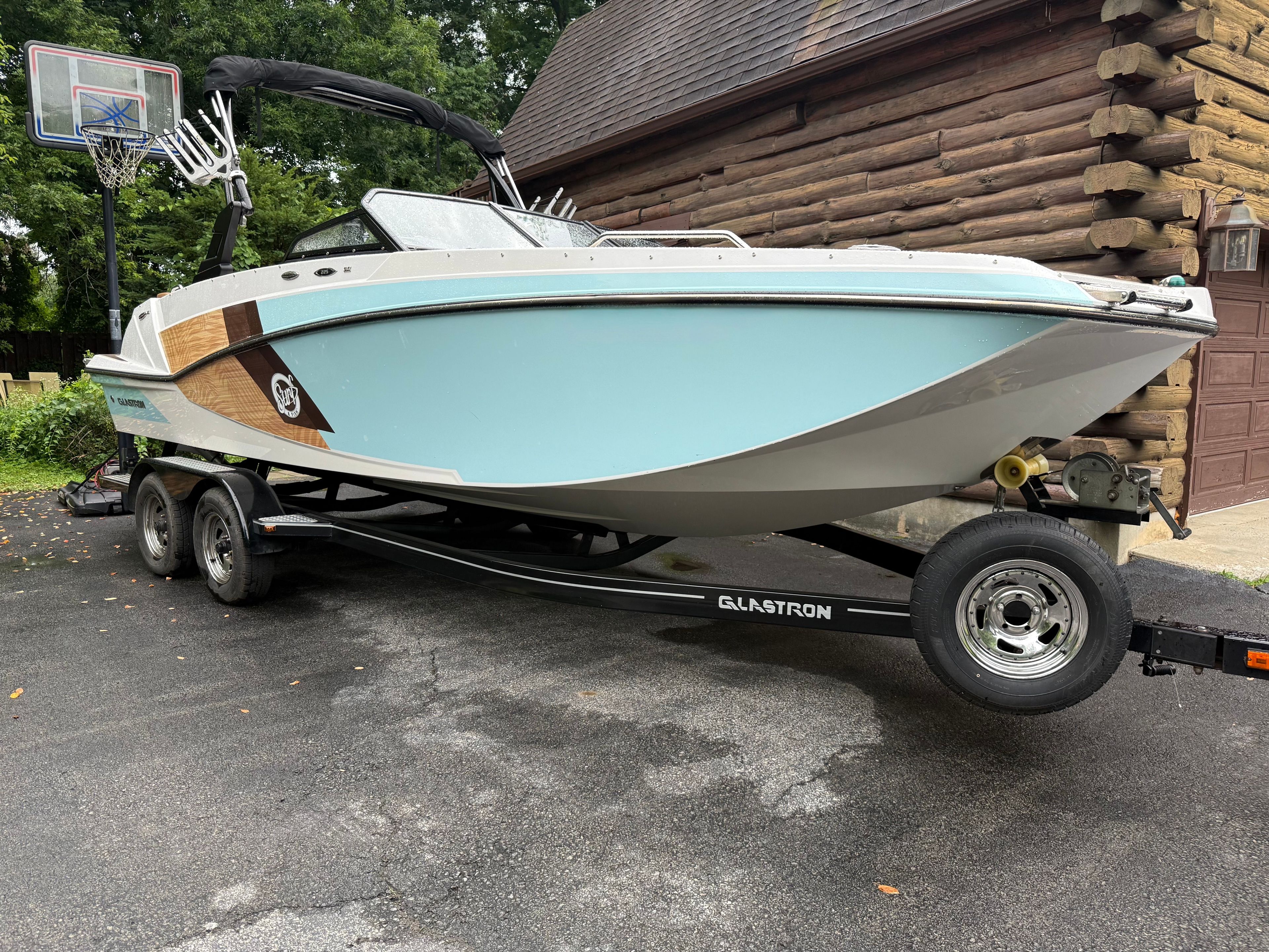 A 2019 Glastron GTDW 225 boat on a trailer beside a log cabin.