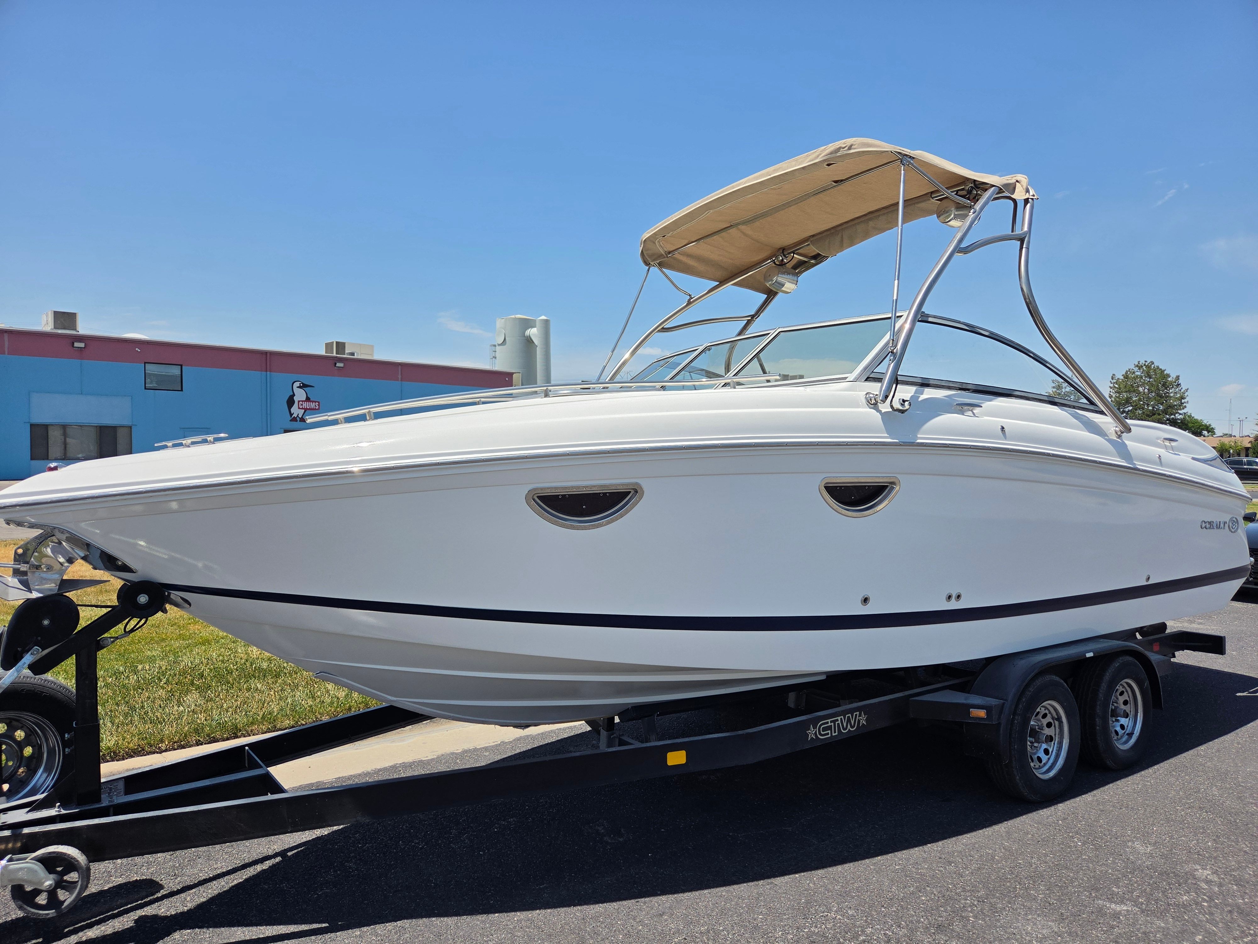 A white Cobalt boat on a trailer, with a beige sunshade, parked on a lot.