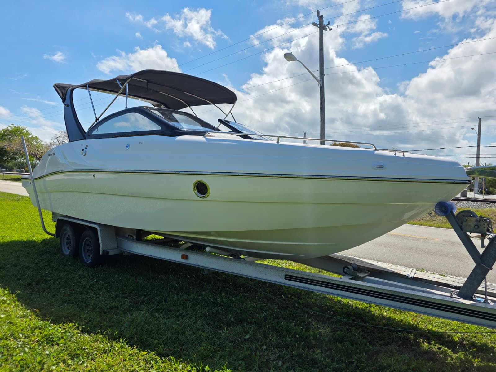 A 2025 Coral 26 boat on a trailer, set on grass under a blue sky.