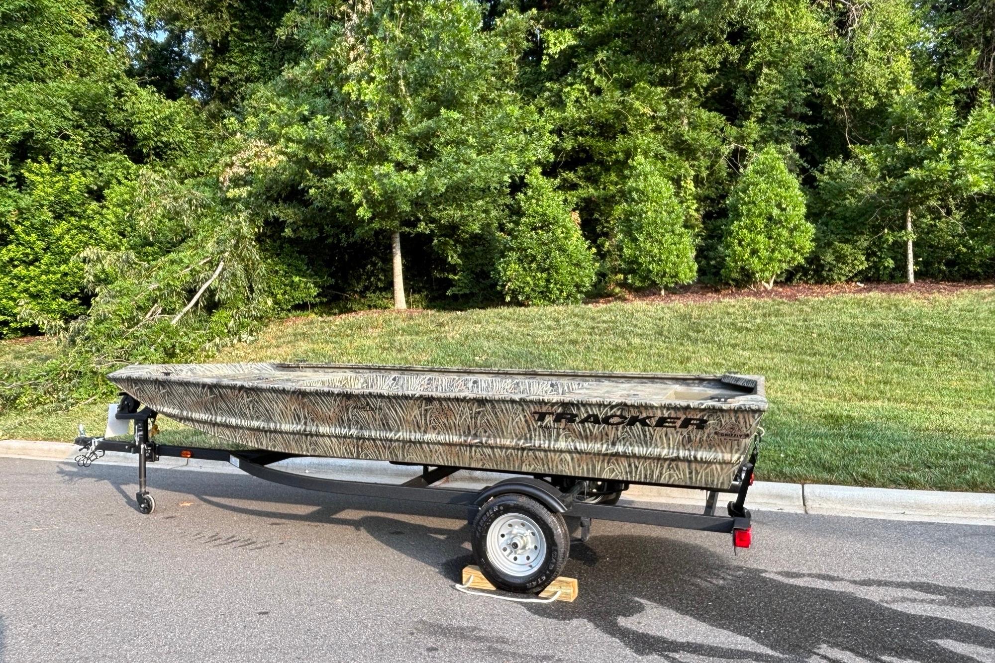 2026 Tracker Grizzly 1648 Utility boat on trailer, parked on a road with greenery background.