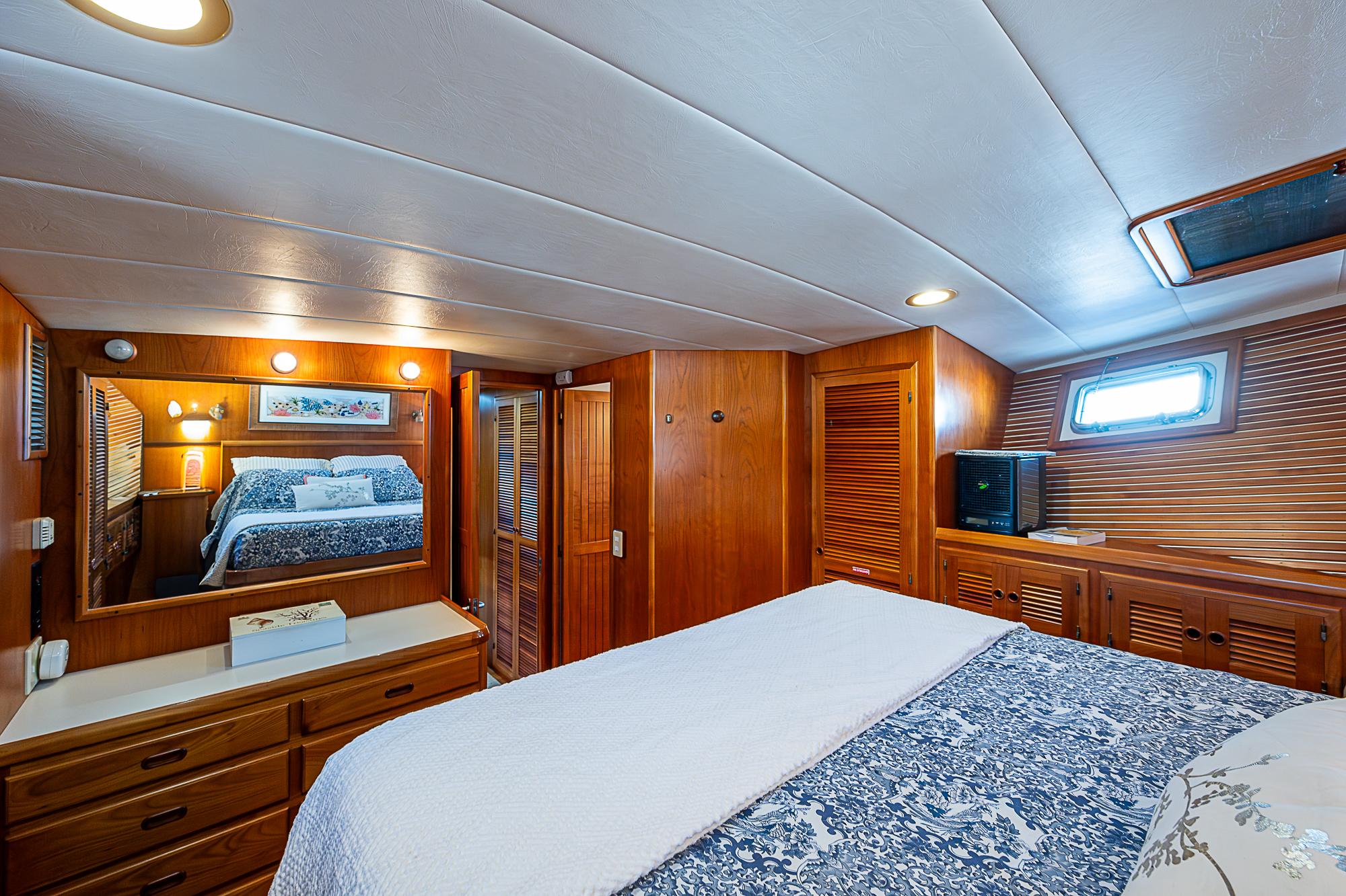 Luxurious wood-paneled bedroom in 2001 Kadey-Krogen 58 yacht, featuring cozy bedding and ample storage.