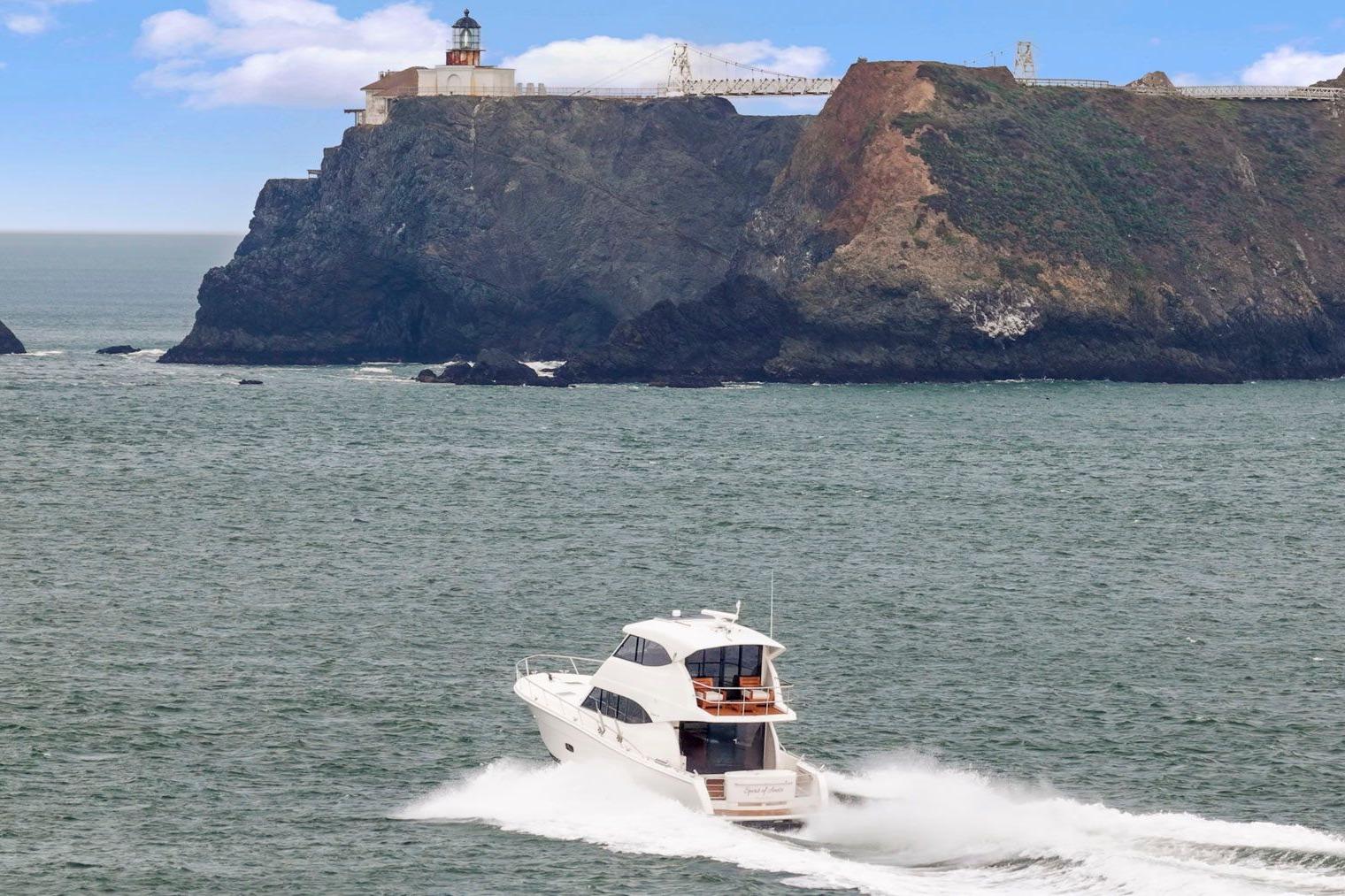 2014 Maritimo M50 yacht cruising near rocky coastline with lighthouse.