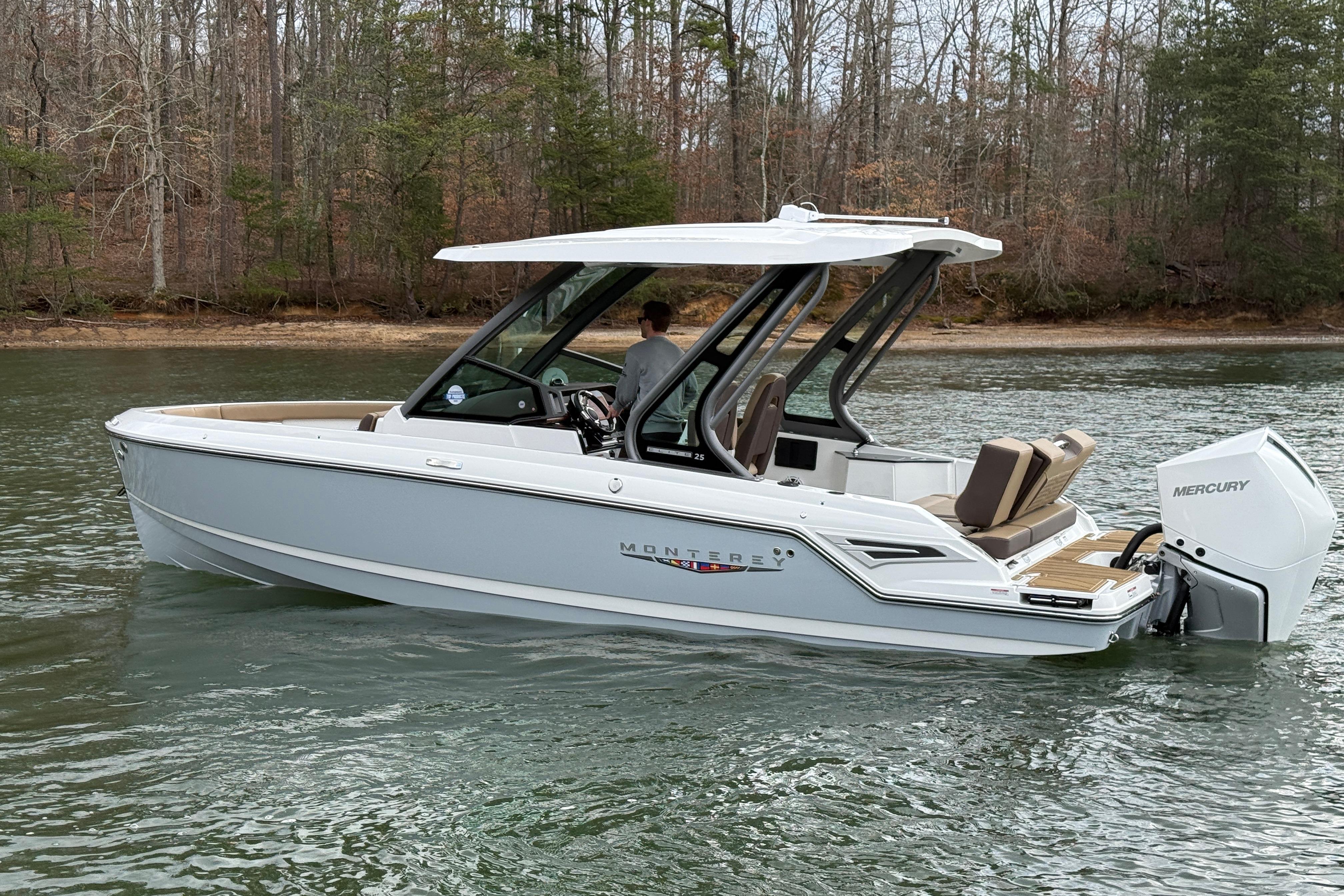 2026 Monterey Elite 25 OB boat on a serene lake with wooded shoreline.