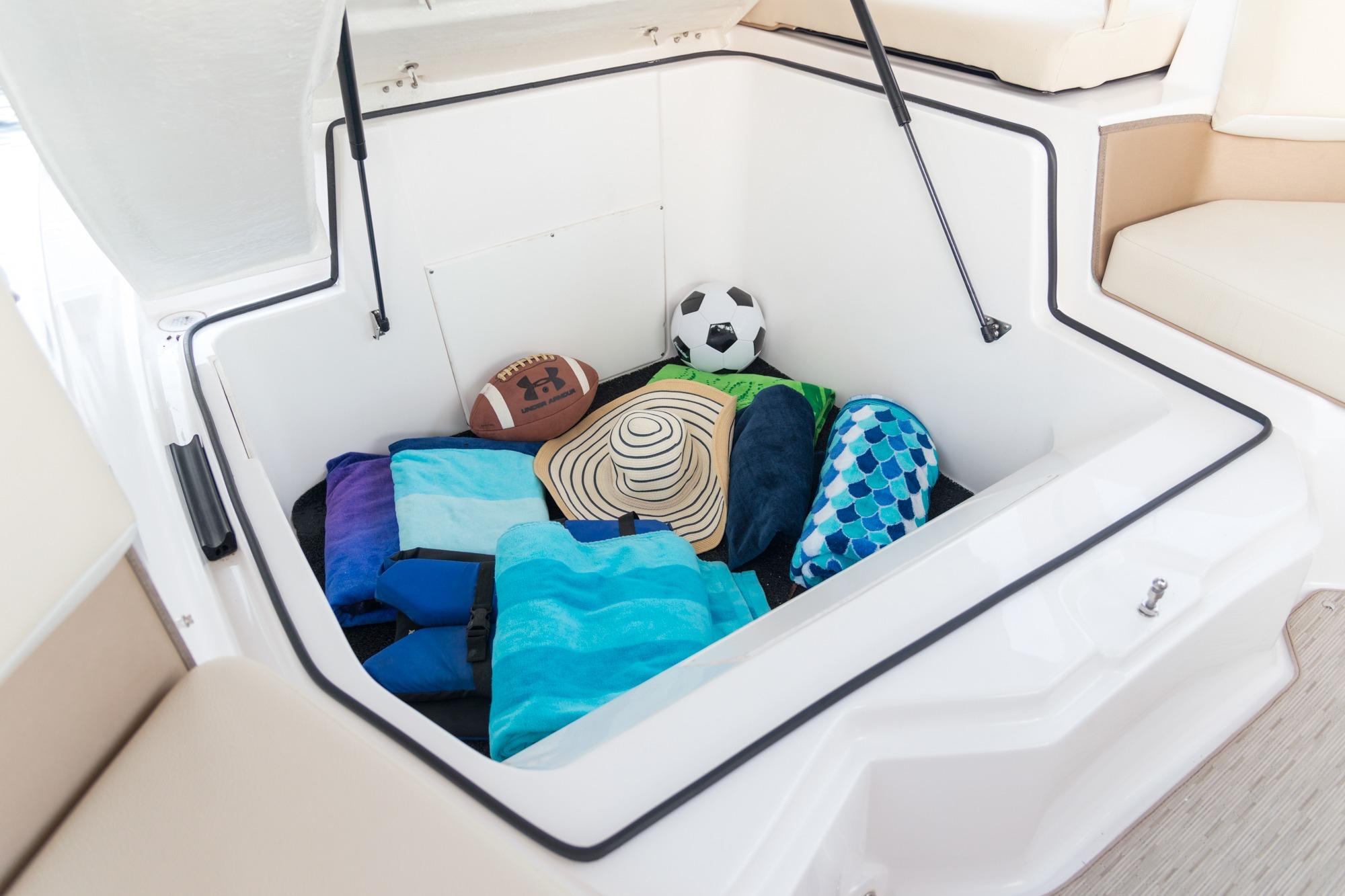 Spacious storage compartment in 2026 Regal 21 OBX boat, filled with sports and beach gear.