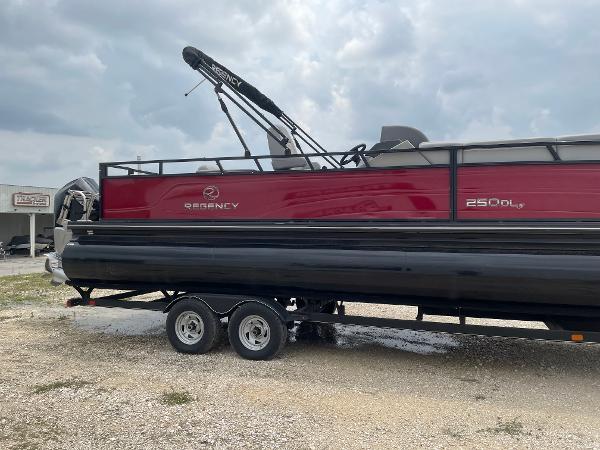 2023 Regency 250DL3 pontoon boat on trailer, red and black design, cloudy sky background.