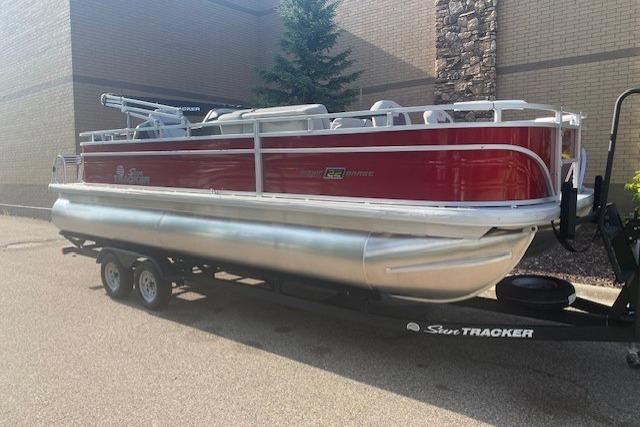 2026 Sun Tracker Fishin' Barge 22 DLX pontoon boat on trailer, parked outdoors.