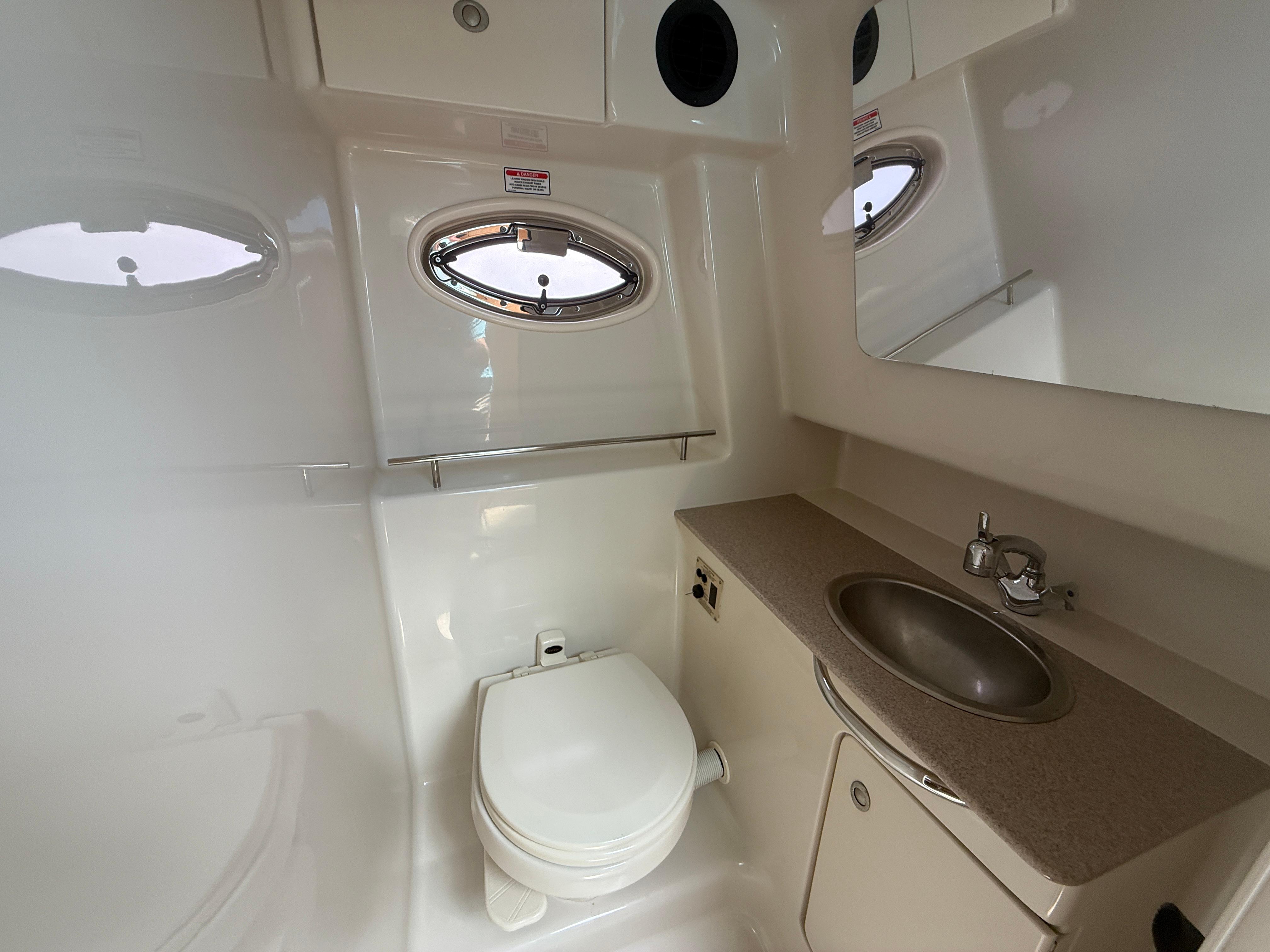 2006 Sea Ray 290 Sundancer bathroom with toilet, sink, and porthole window.