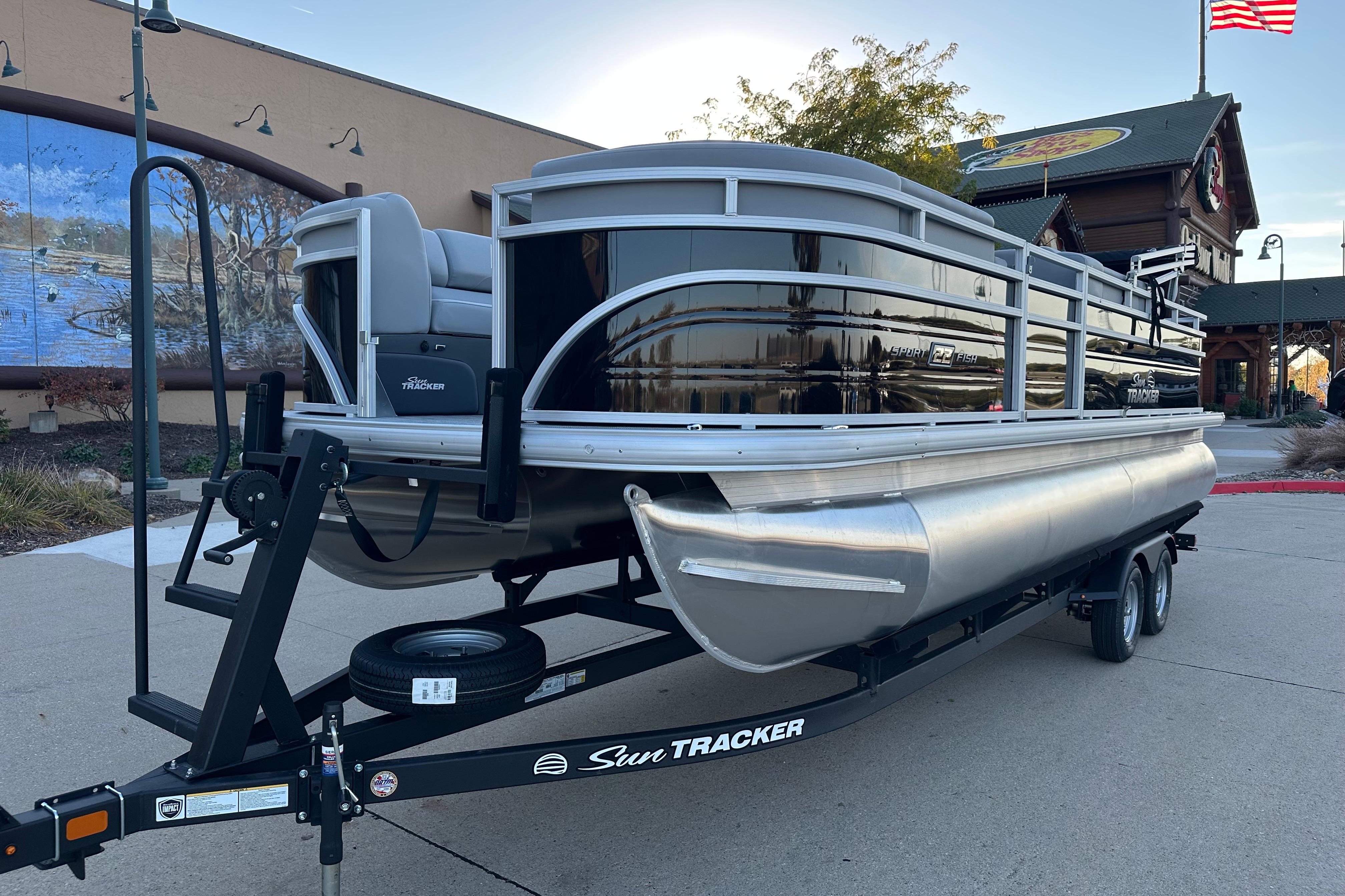 2026 Sun Tracker SportFish 22 DLX pontoon boat on trailer, parked outdoors.