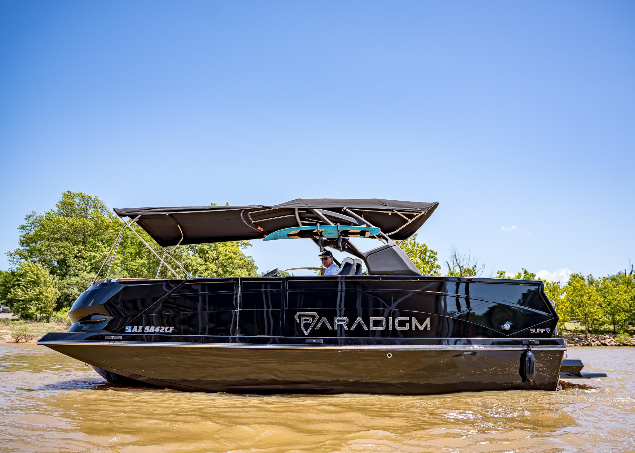2025 Paradigm 236 boat cruising on a sunny day with lush greenery in the background.
