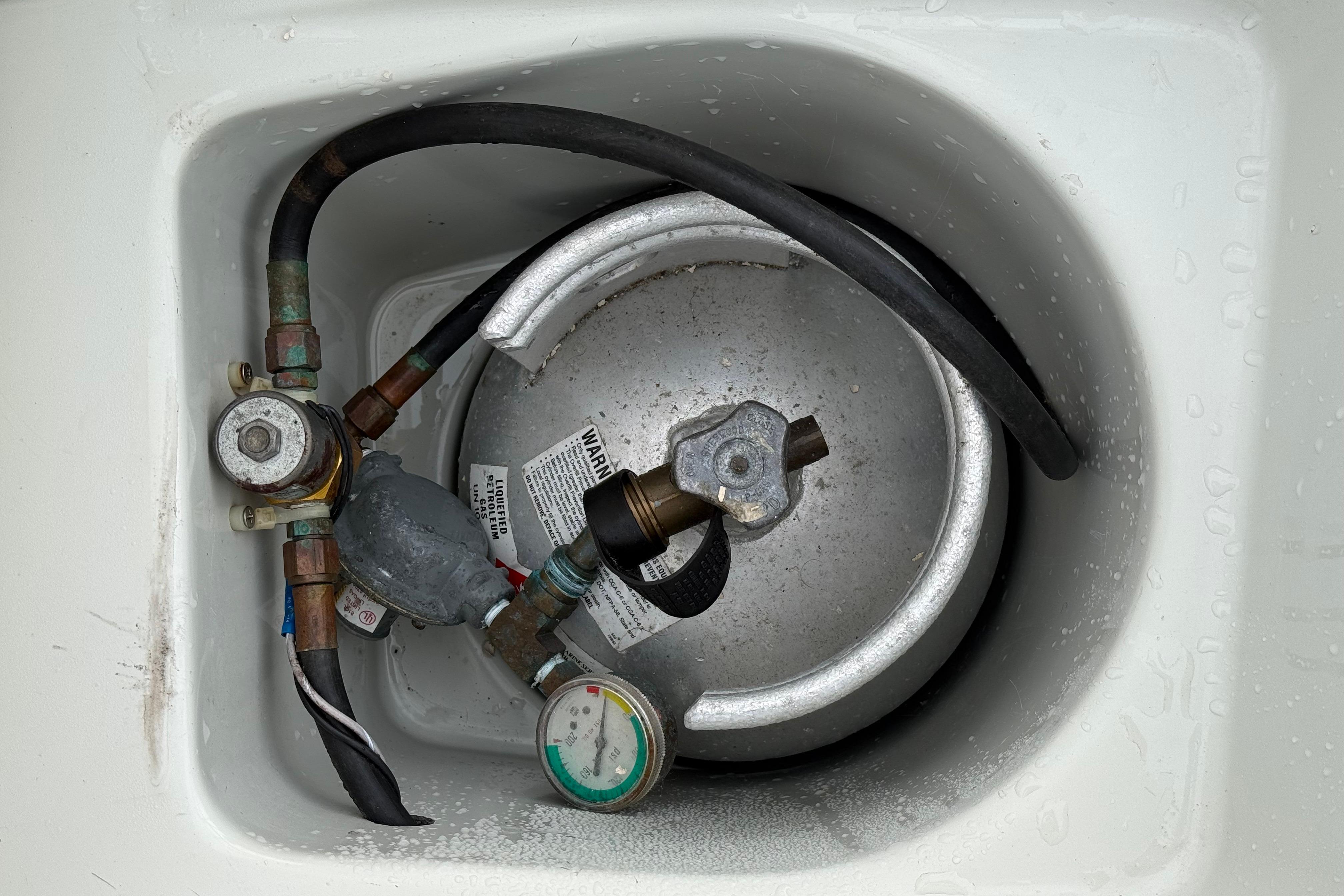 Propane tank setup in Ericson 32-200 sailboat, 1988 model, with connected hoses and gauge.