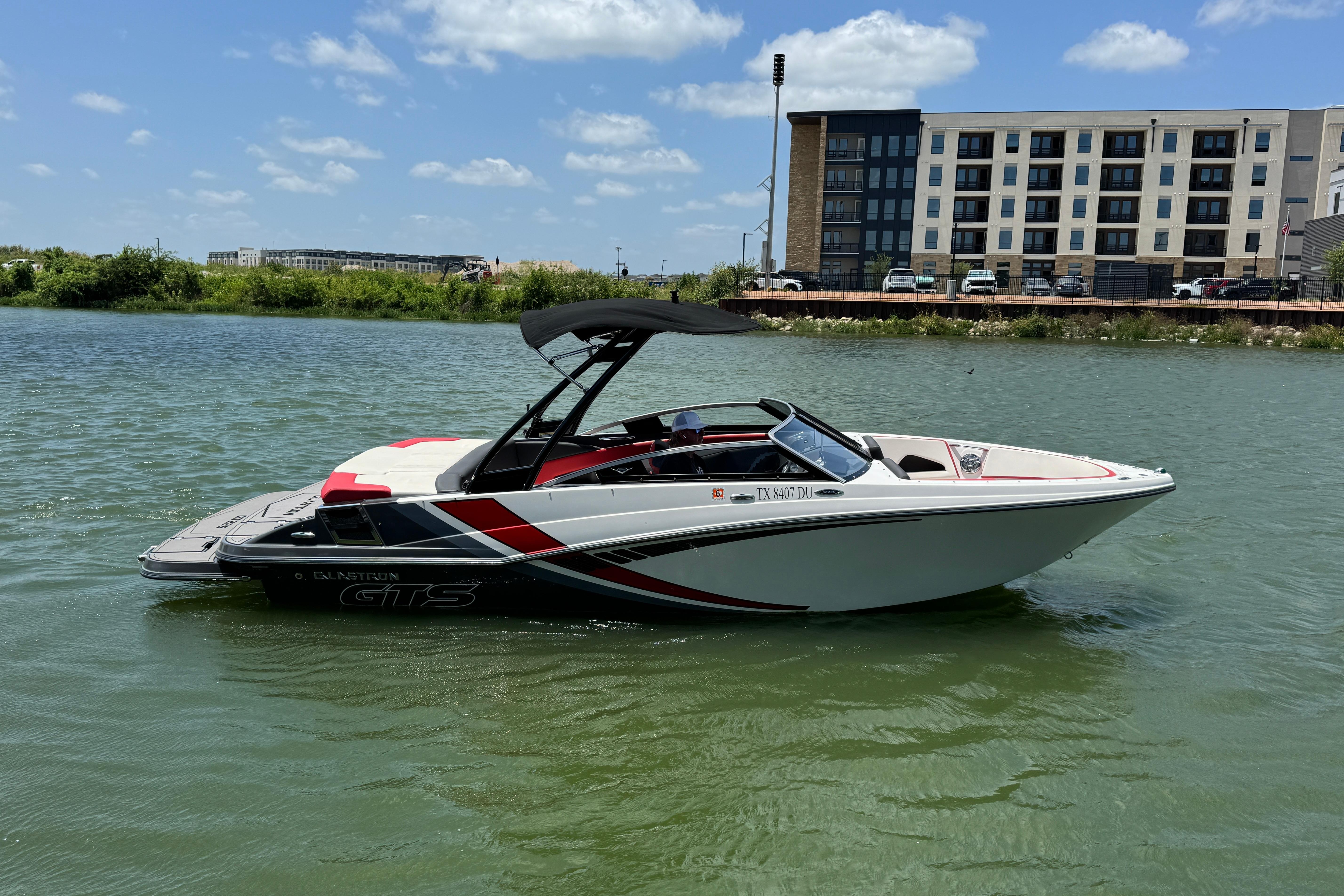2017 Glastron GT 225 boat on water, modern design, near urban buildings under blue sky.