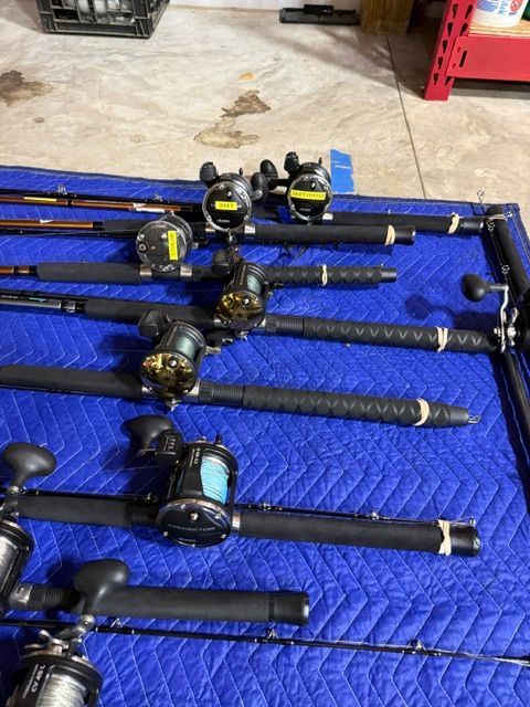 Several fishing rods with reels are laid out on a blue blanket.
