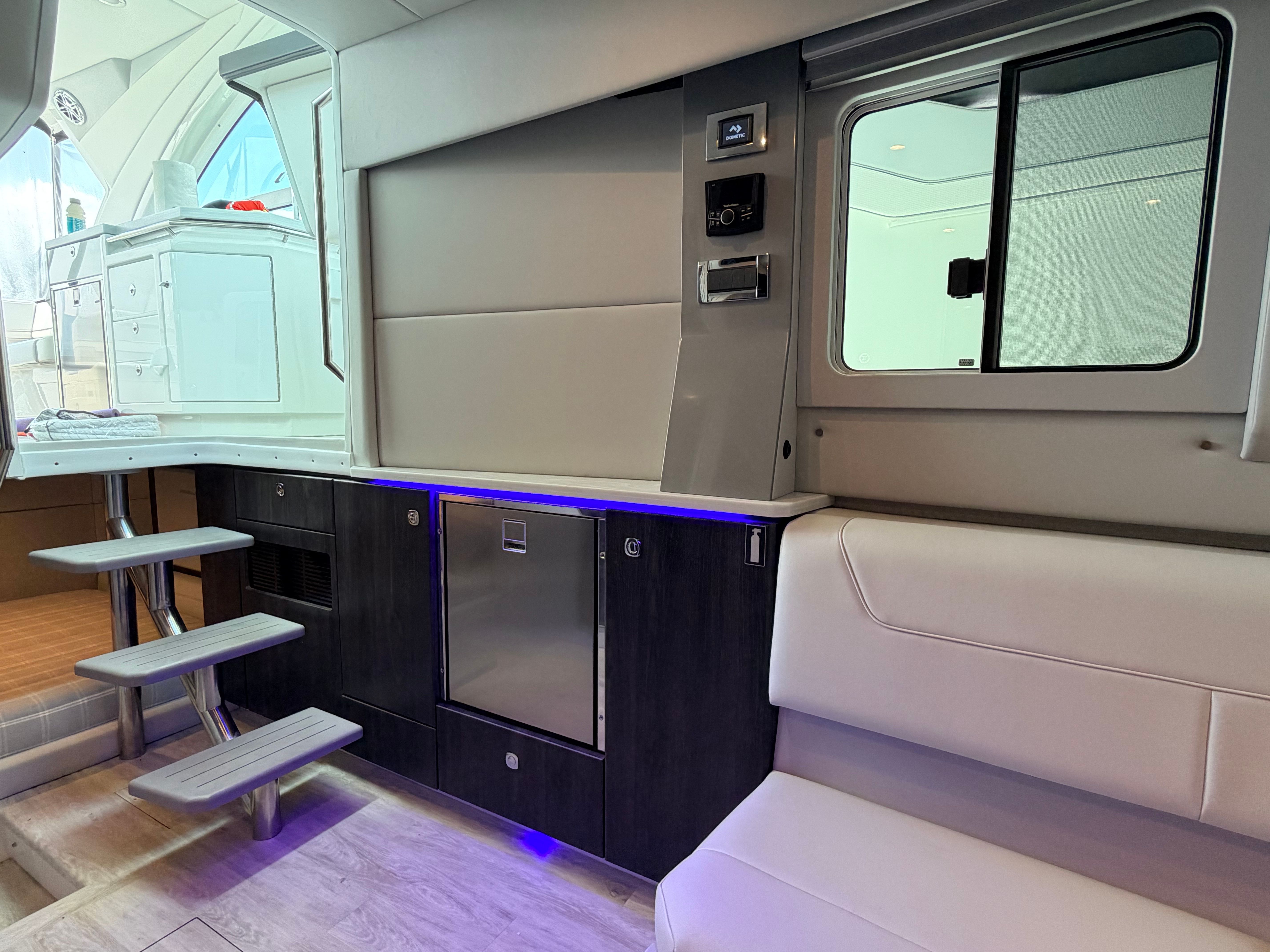 Interior of a modern yacht with sleek seating, stairs, and a refrigerator.