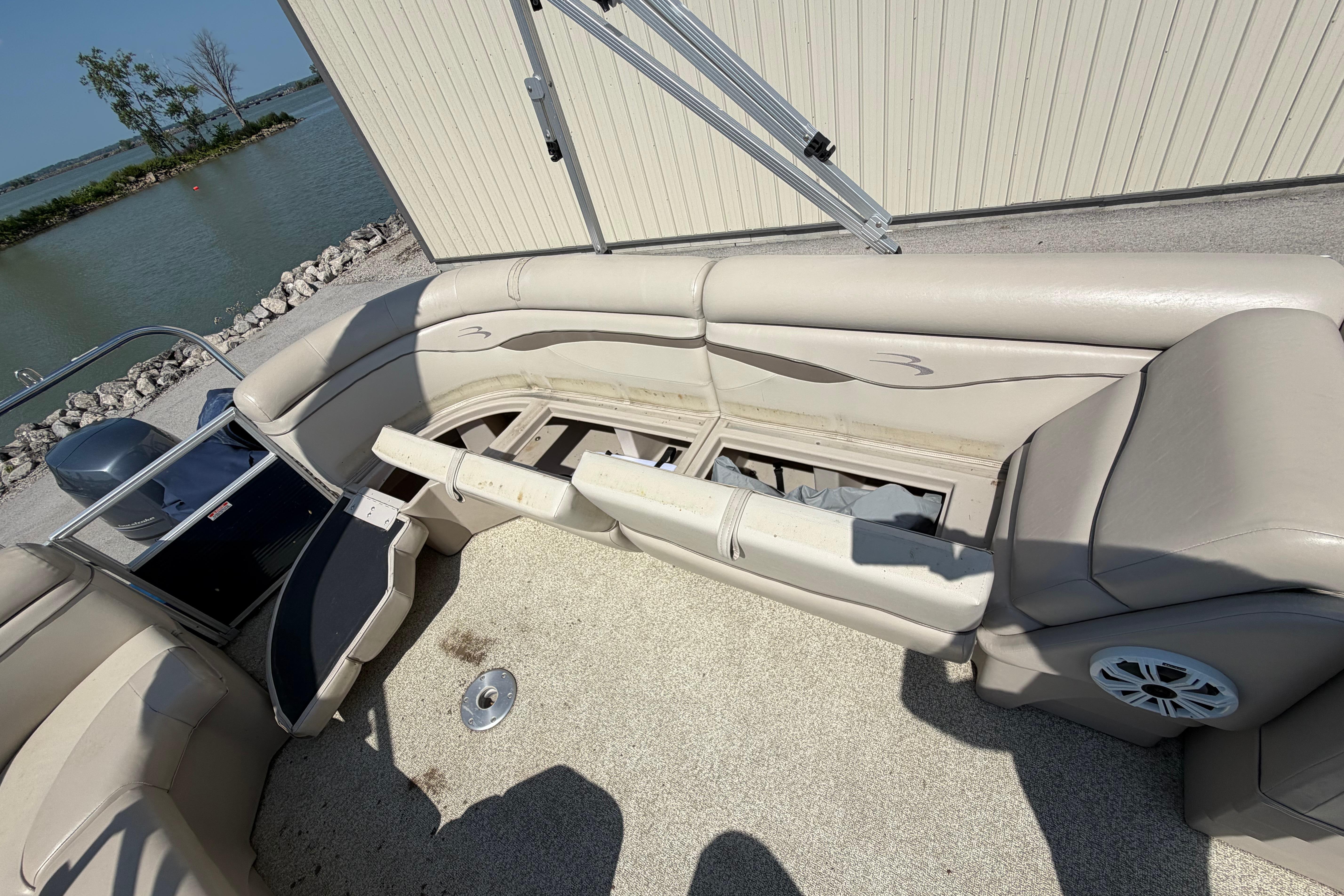 2017 Bennington 25 SSXAPG pontoon boat interior with open storage compartments by a lakeside.