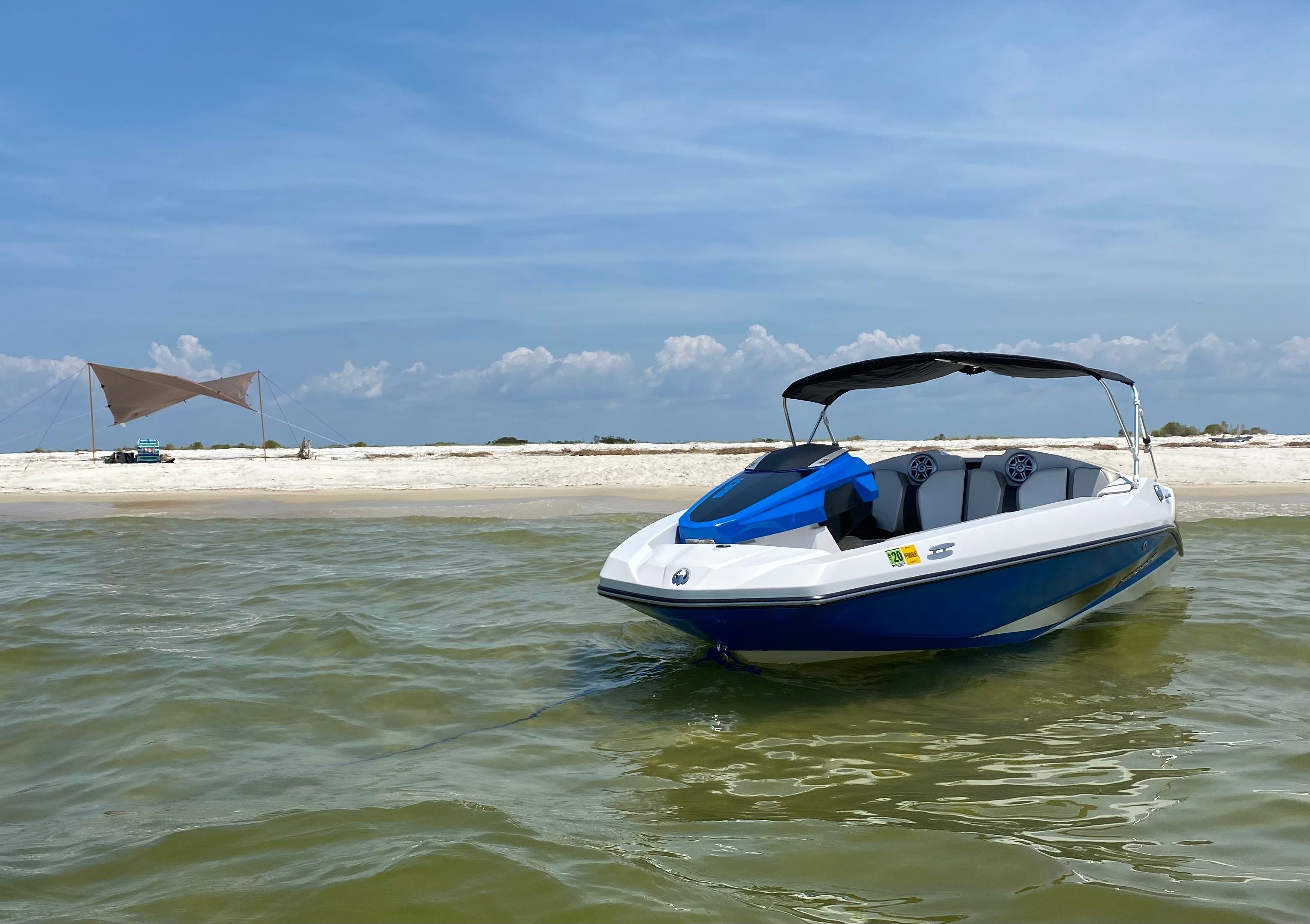A 2015 Scarab 165 boat sits in shallow water near a sandy beach.