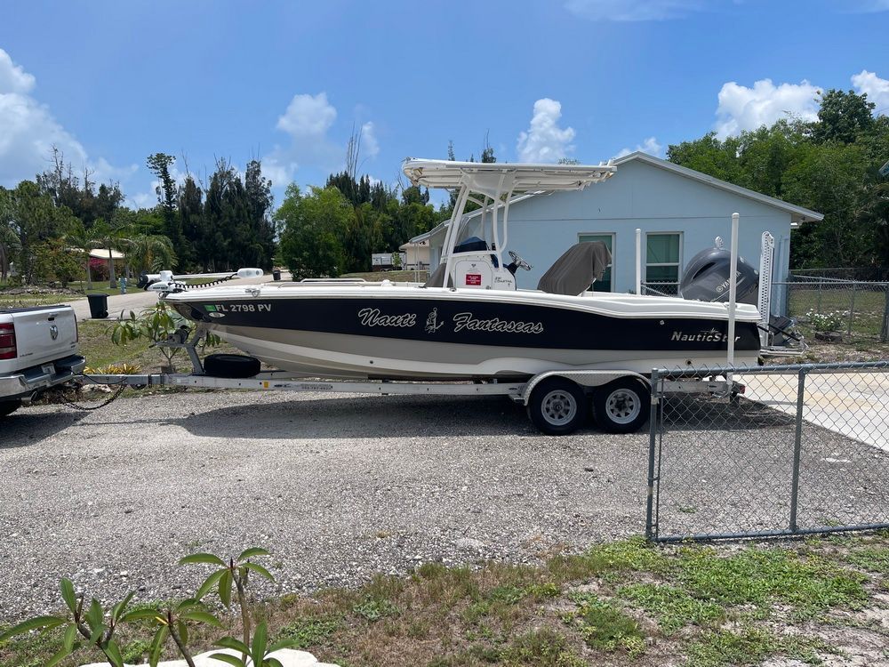 A 2015 NauticStar 231 Coastal boat on a trailer in a yard next to a house.