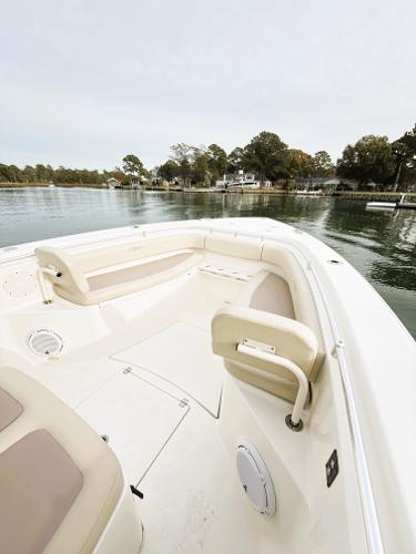 2016 Cobia 296 Center Console boat on calm water, featuring spacious seating and scenic shoreline.