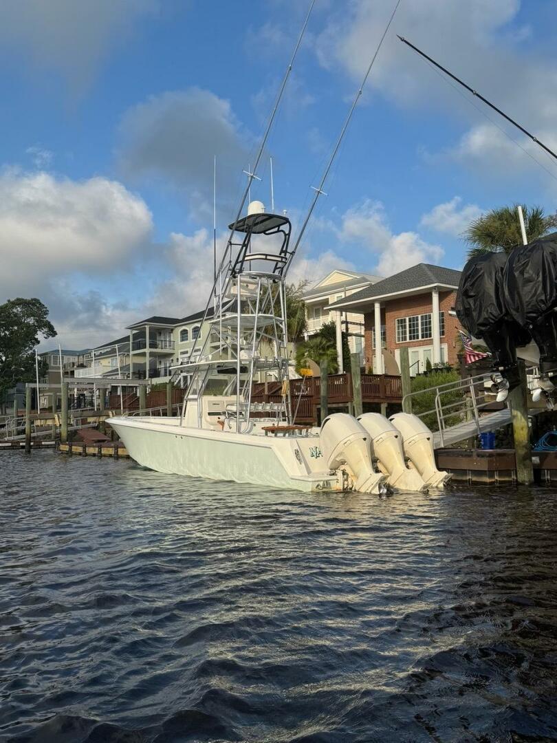 2012 Contender 39ST boat docked by waterfront homes under a blue sky.