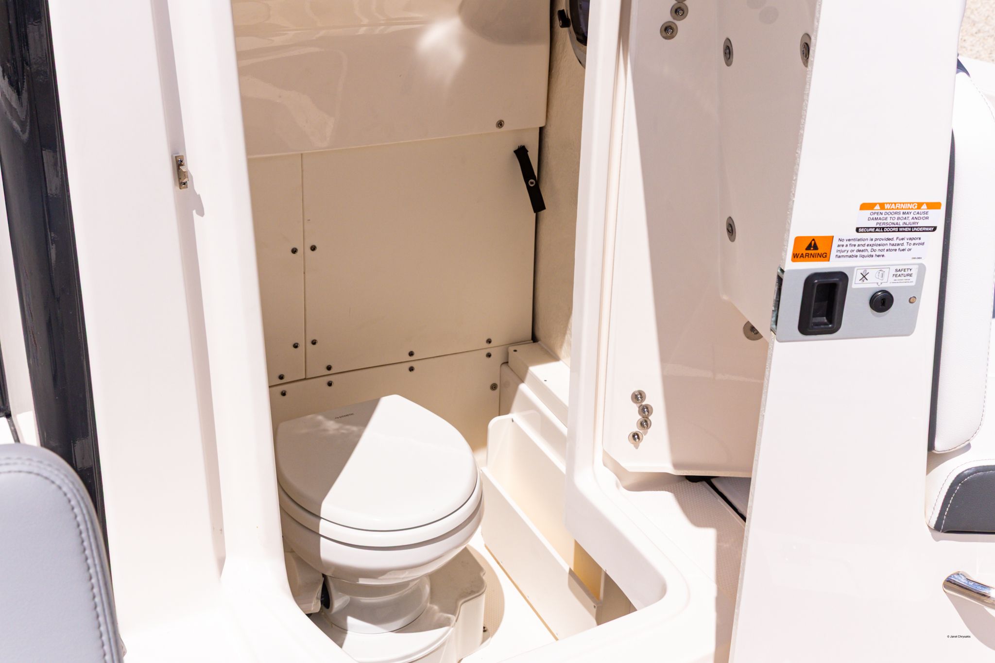 Interior view of a boat toilet with white walls and a seat.