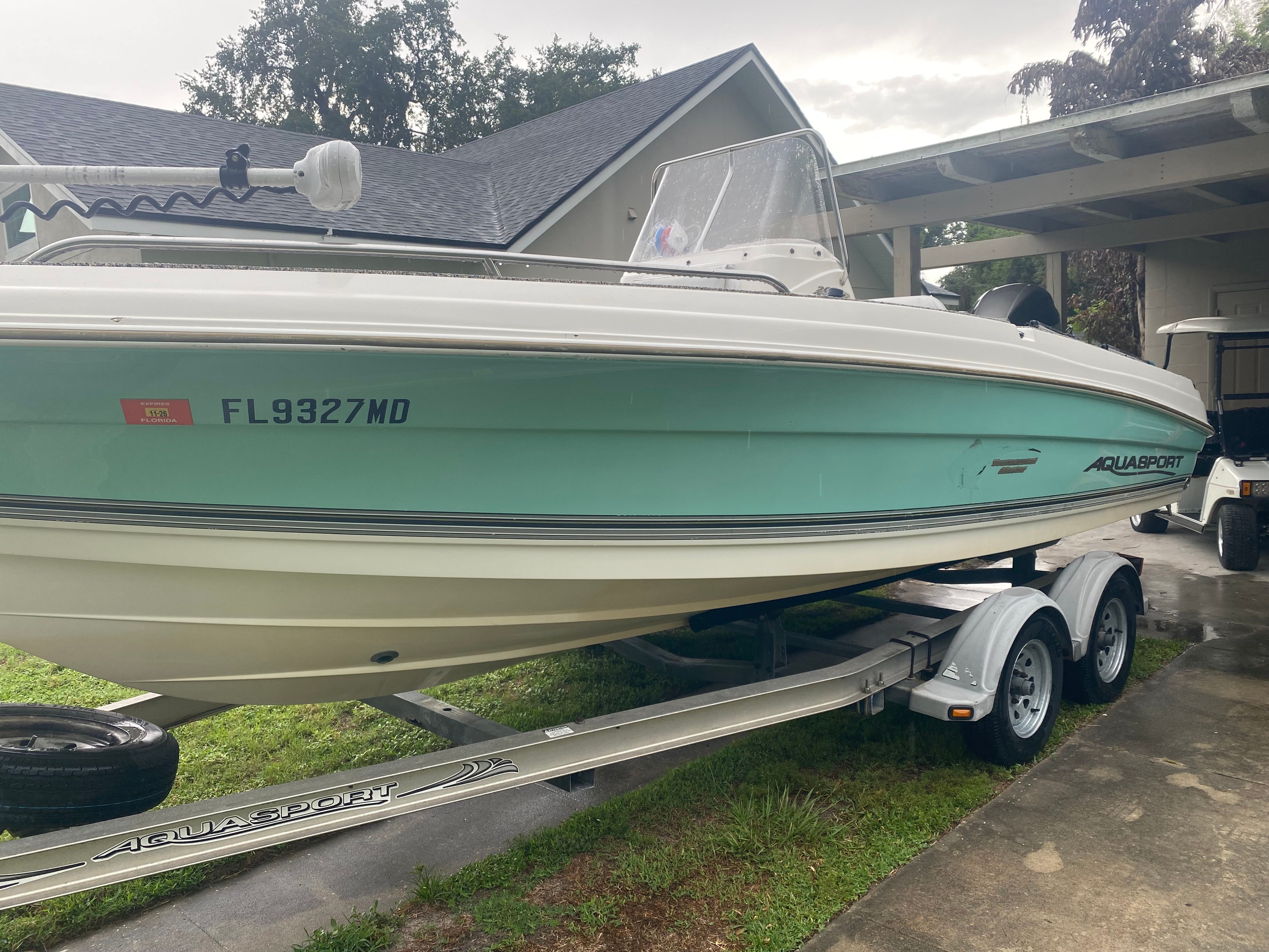 A 2003 Aquasport 201 Osprey boat on a trailer in a driveway.