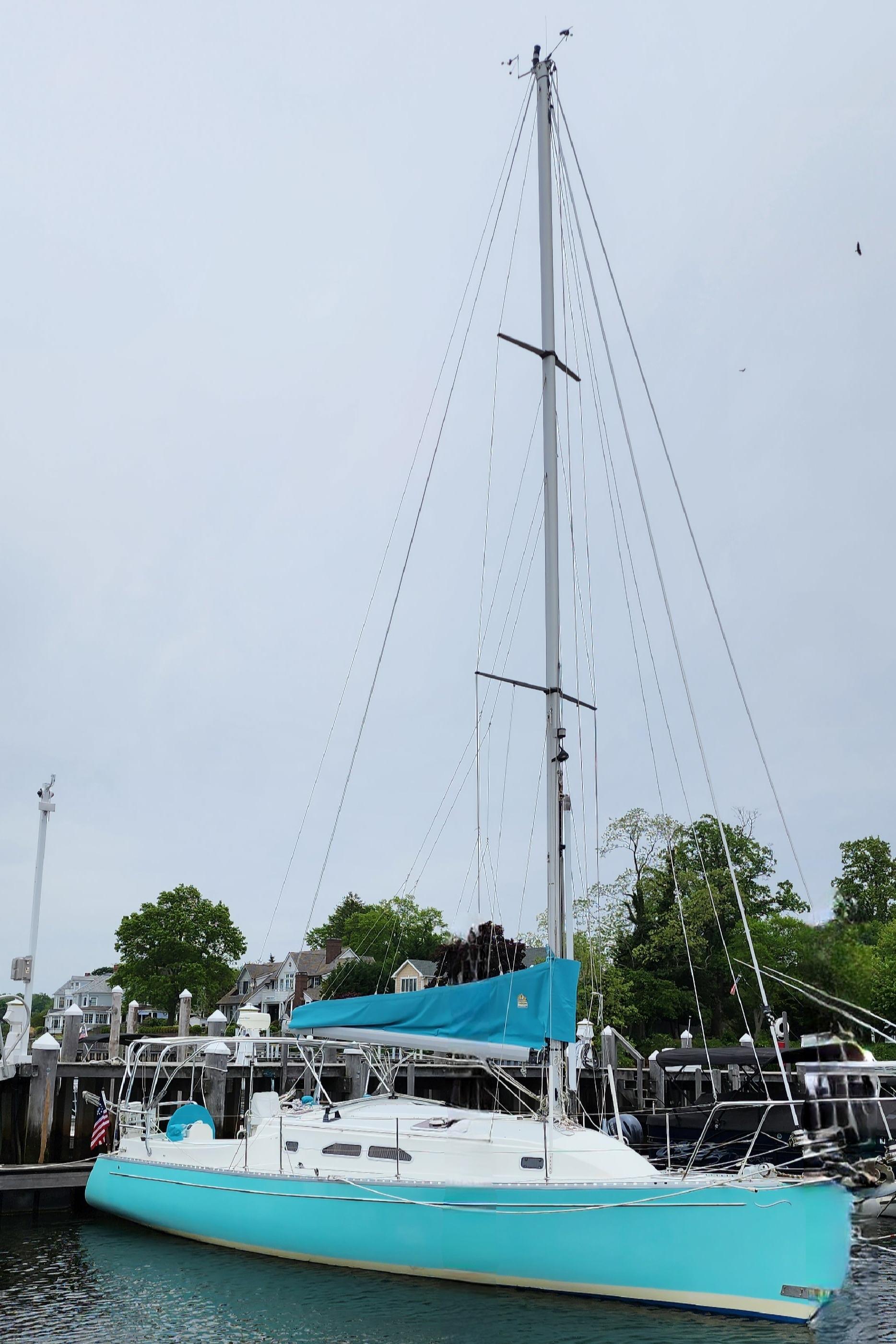 2005 Shannon Shoalsailer sailboat docked, featuring a turquoise hull and tall mast.