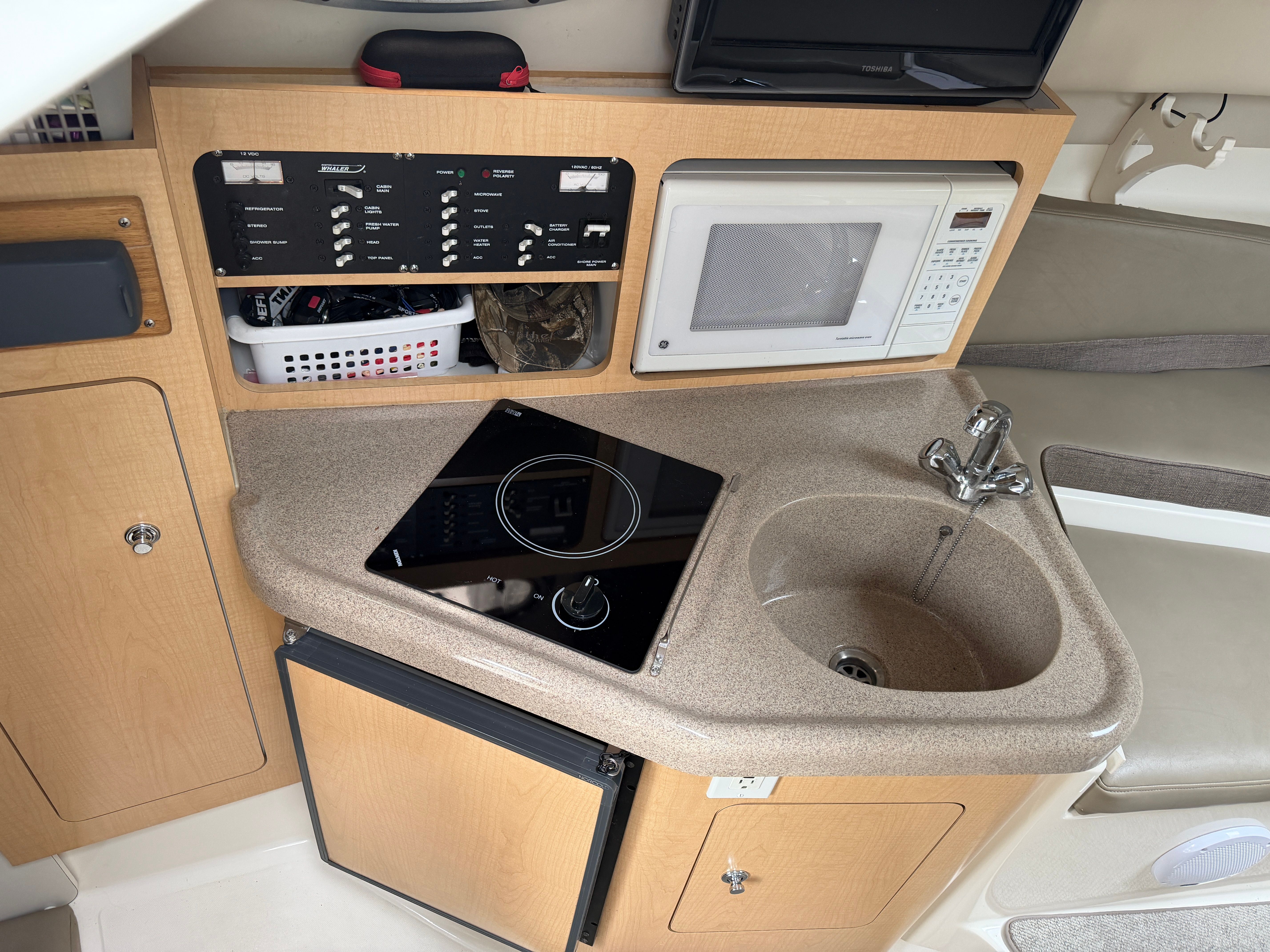 Compact galley with sink, stove, microwave, and fridge inside a boat.
