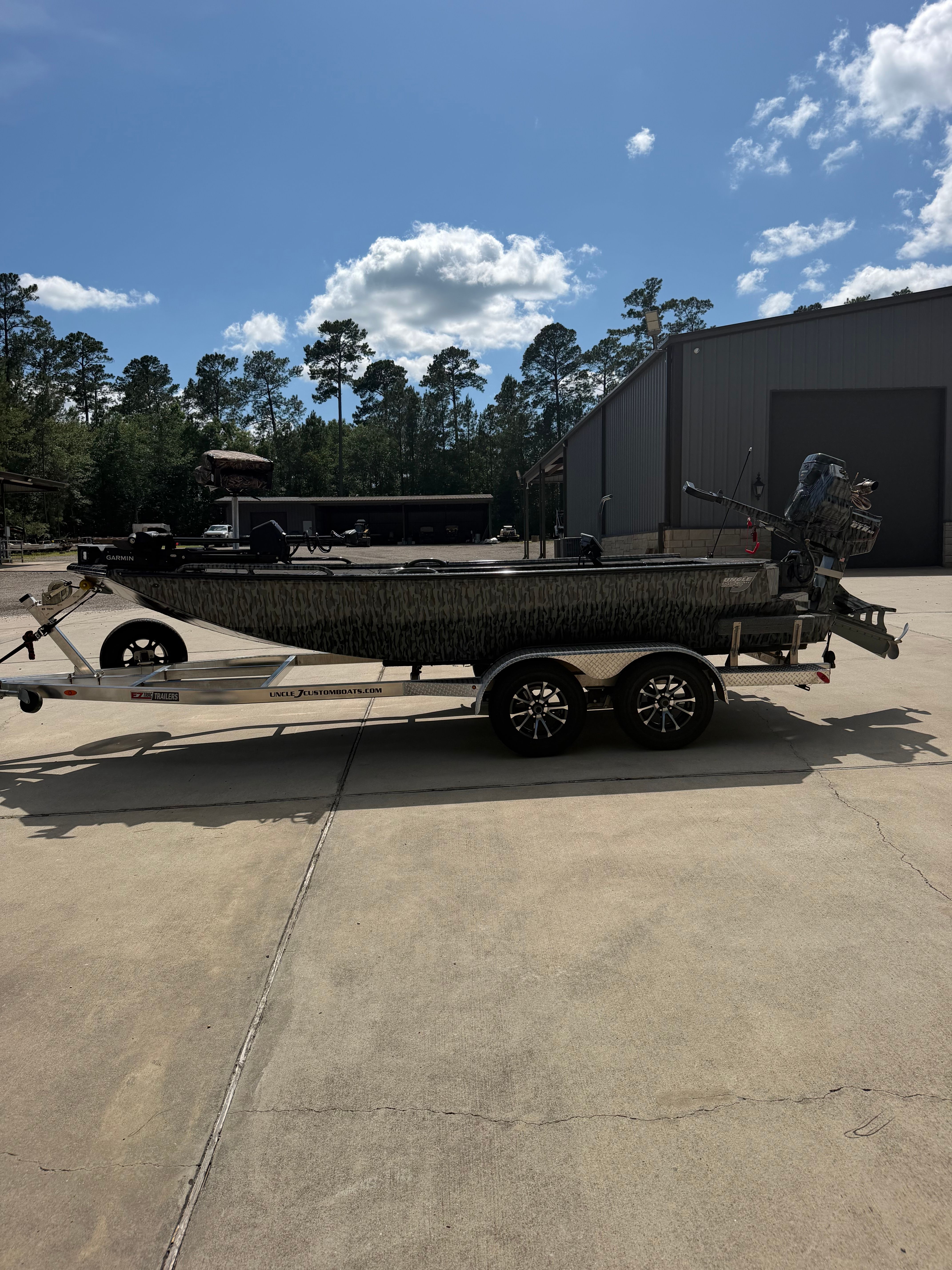 A boat on a trailer sits on a concrete lot in front of a building.