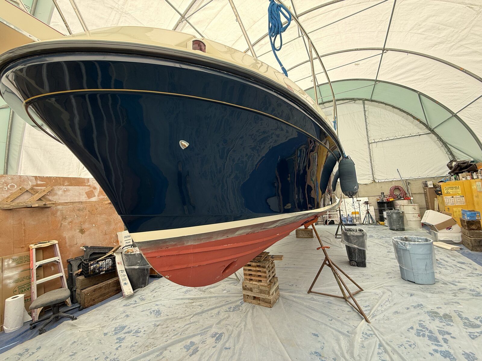 A blue boat in dry dock, surrounded by tools and materials.